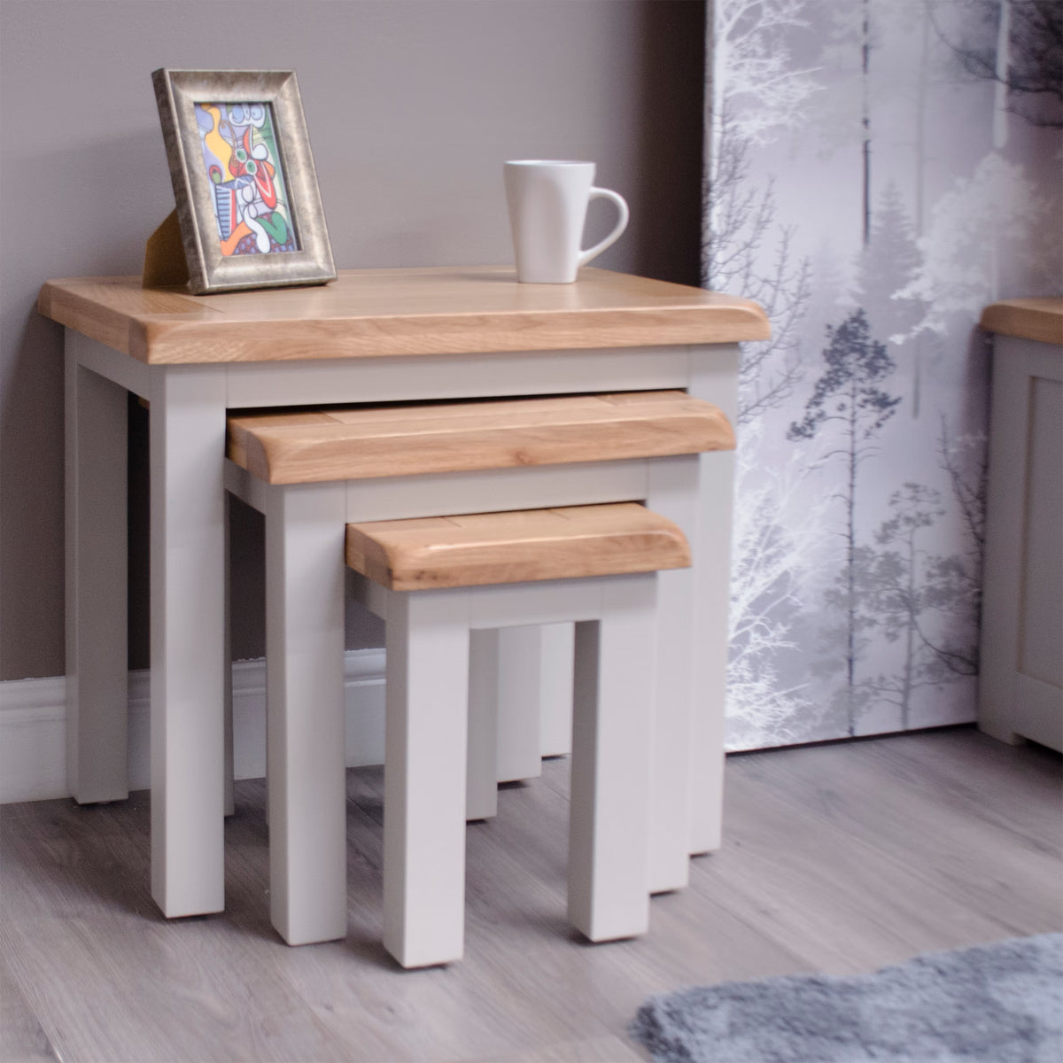Set of three oak and painted nesting tables with frame and mug in modern living room