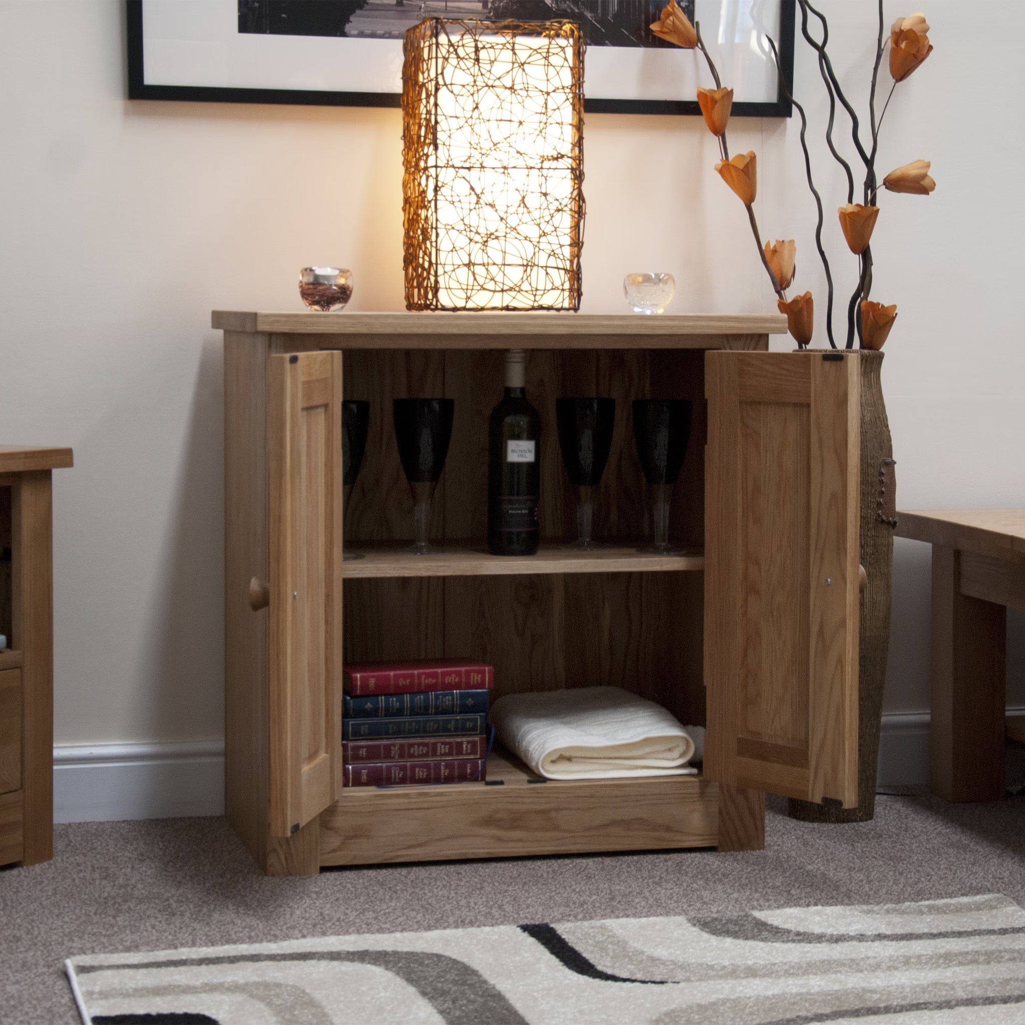Oak sideboard cabinet with open doors, wine glasses, books, and lamp on top