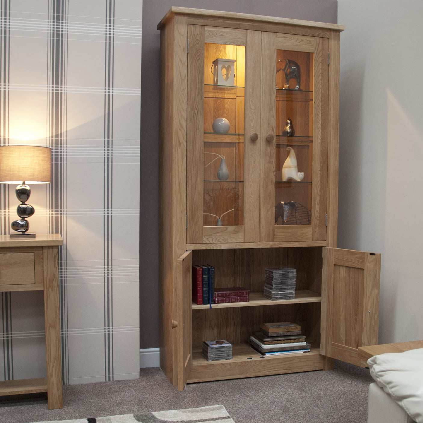 Tall oak display cabinet with glass doors, lower storage shelf and visible decorative items