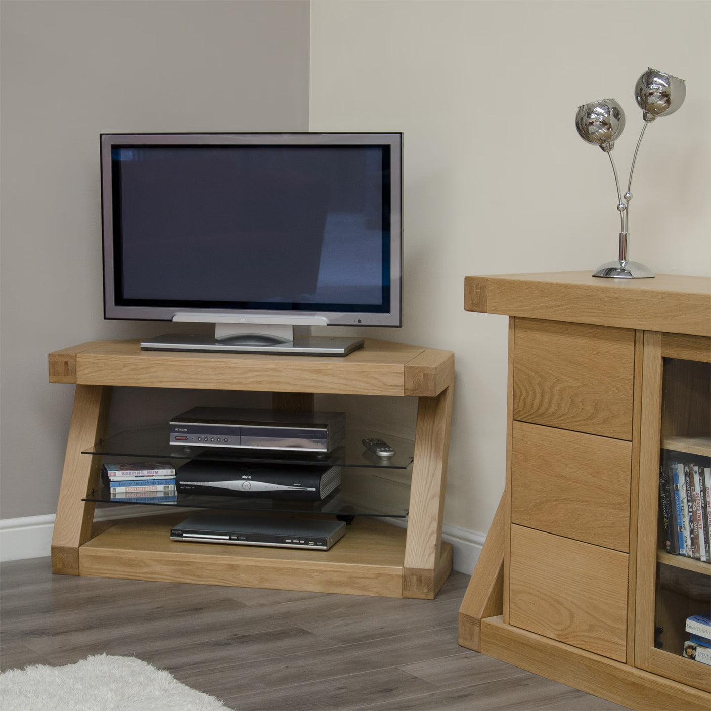 Oak TV stand with glass shelves holding media devices in modern living room corner