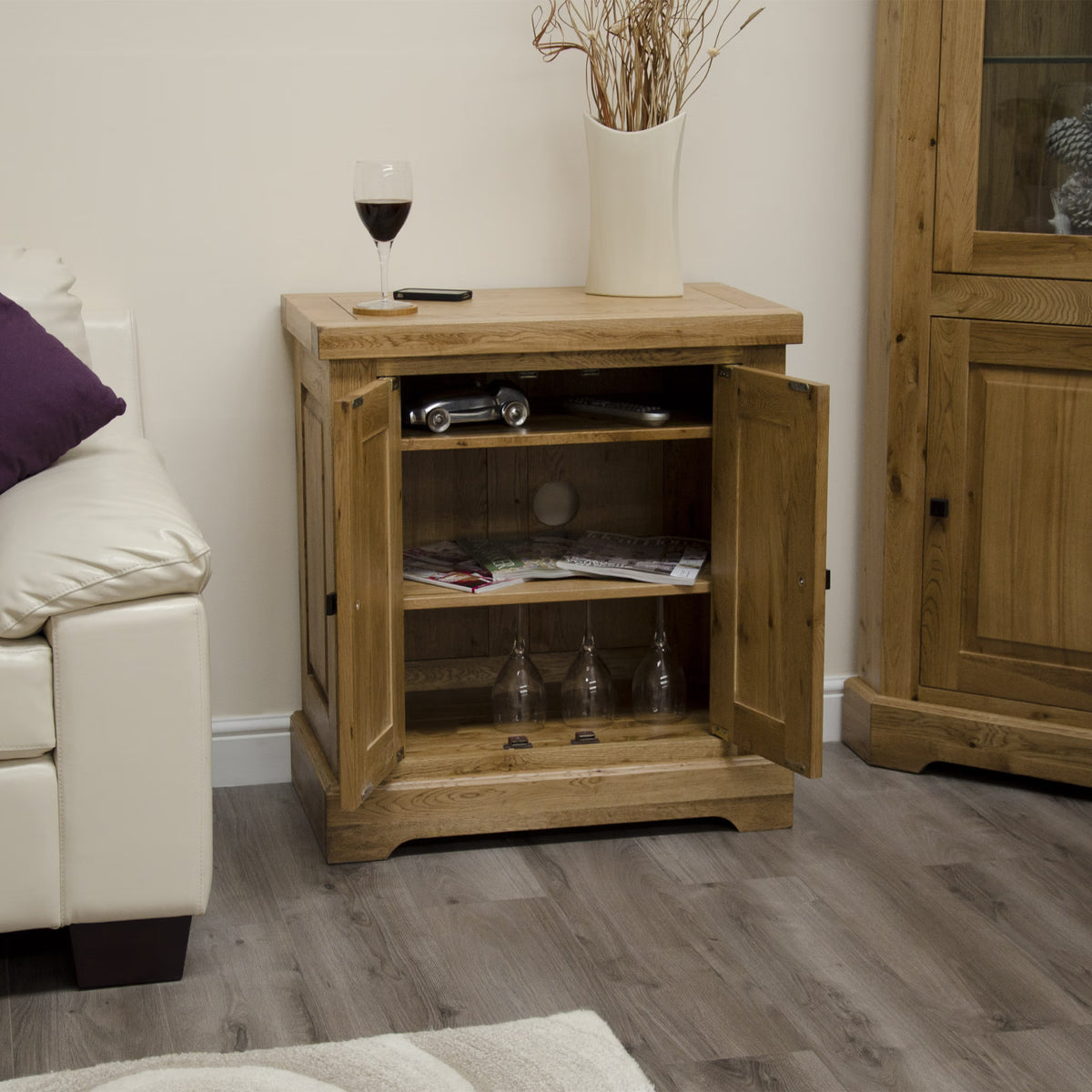 Oak sideboard cabinet with two doors open, glassware inside, on wood floor in living room