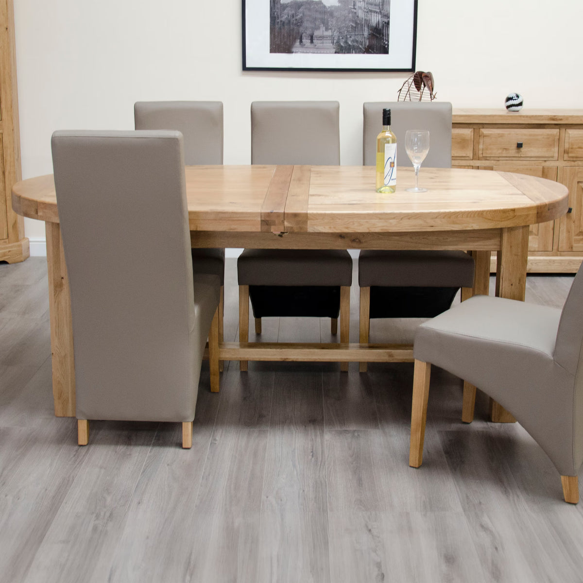Oak dining table with six taupe upholstered chairs on grey wood floor