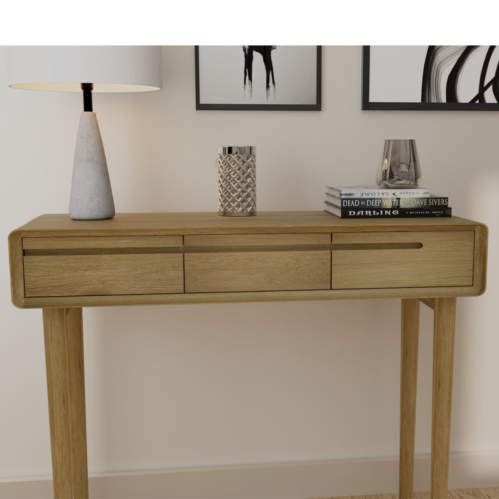 Oak console table with three drawers, table lamp, books and decor against neutral wall