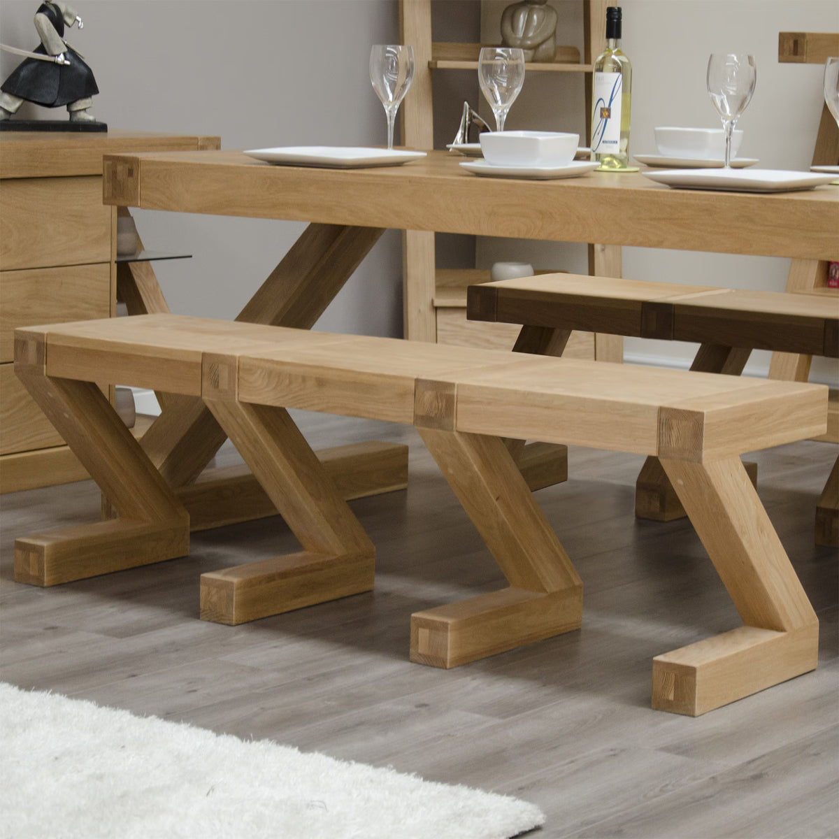 Oak dining bench with modern angled legs next to matching dining table on wooden floor