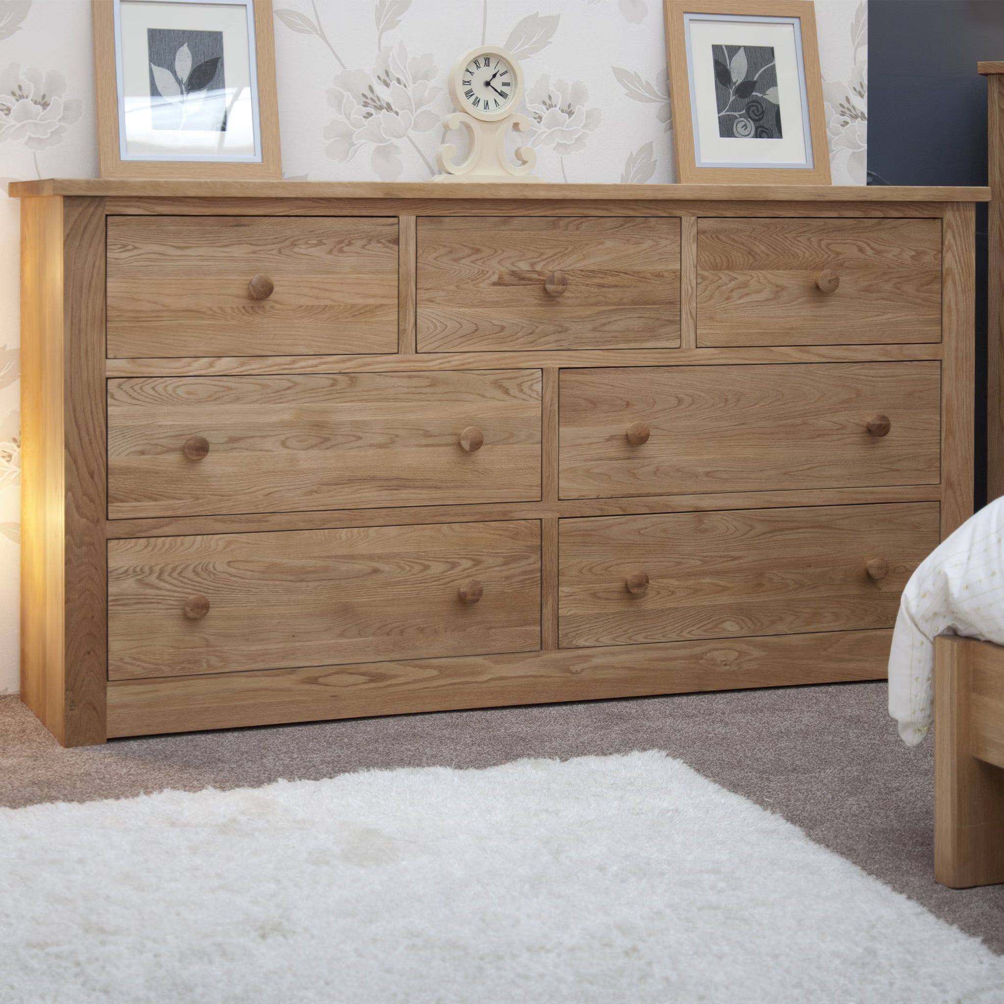Oak chest of drawers with seven handles in bedroom, photos and clock displayed on top