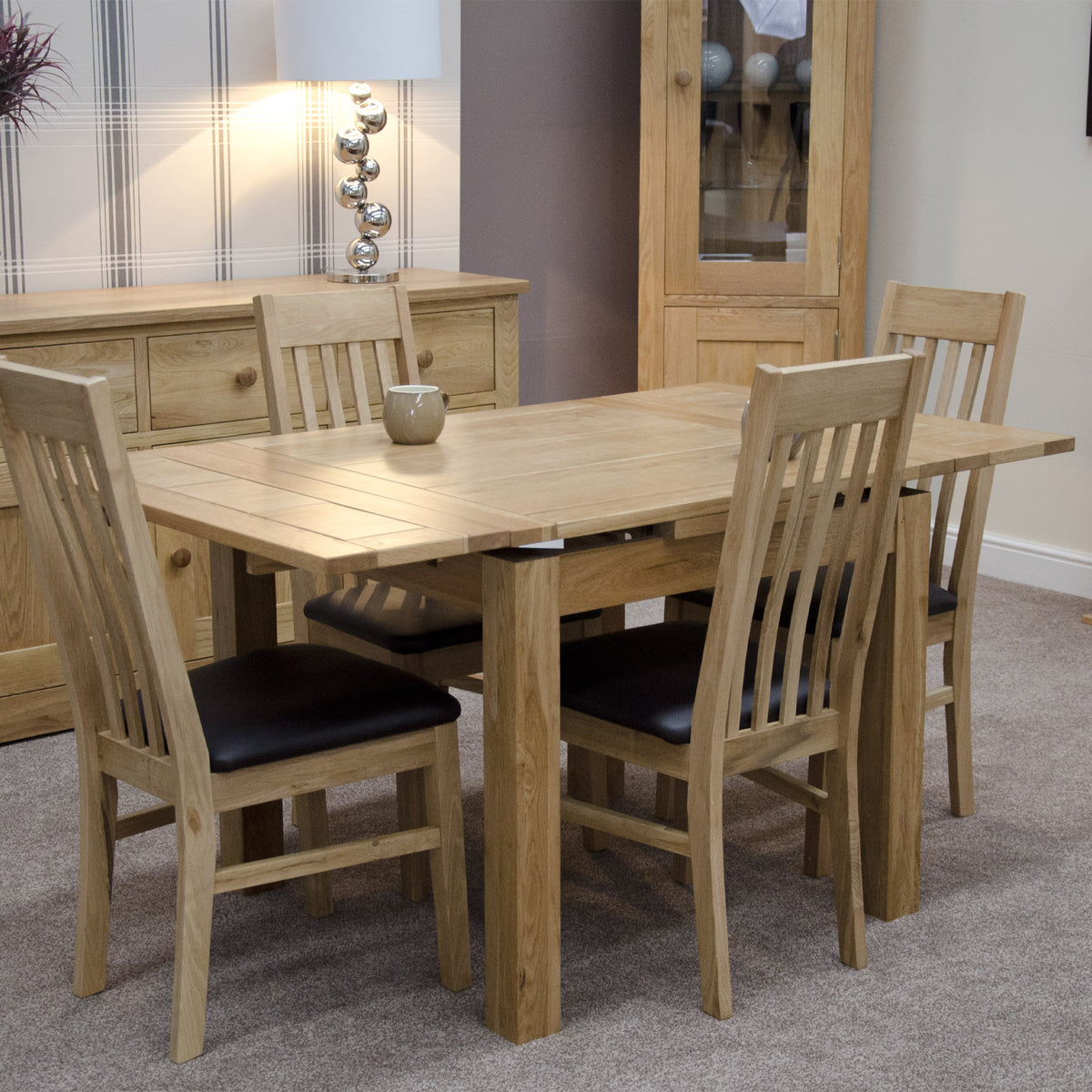 Oak dining table set with four chairs and black seat pads in a carpeted dining room