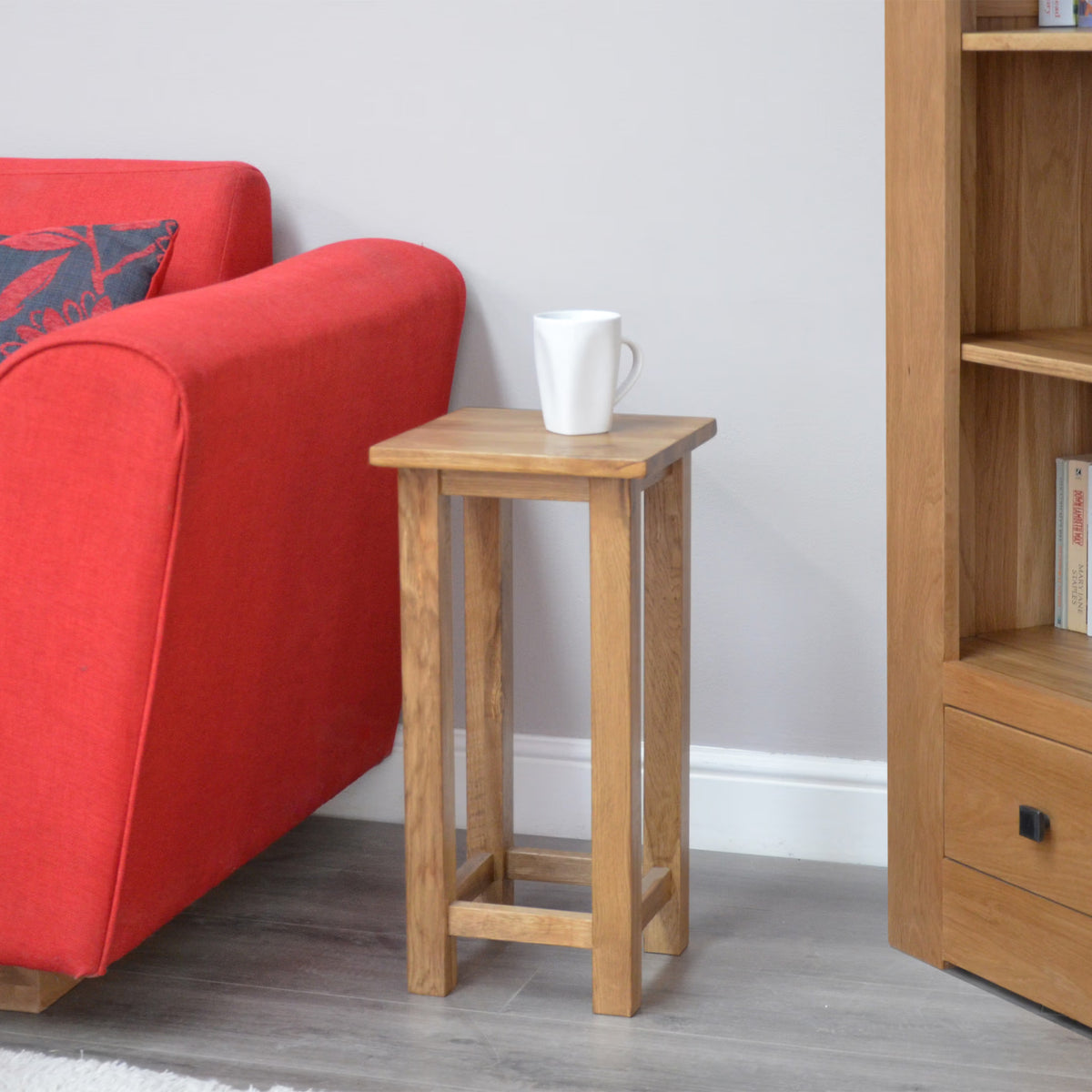 Oak lamp table beside red sofa with mug, positioned on grey wood floor next to bookshelf