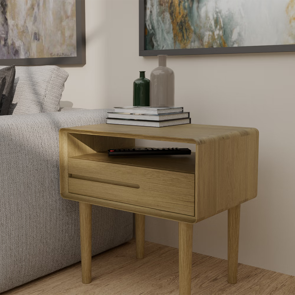 Oak bedside table with drawer and open shelf beside sofa, books and vases on top