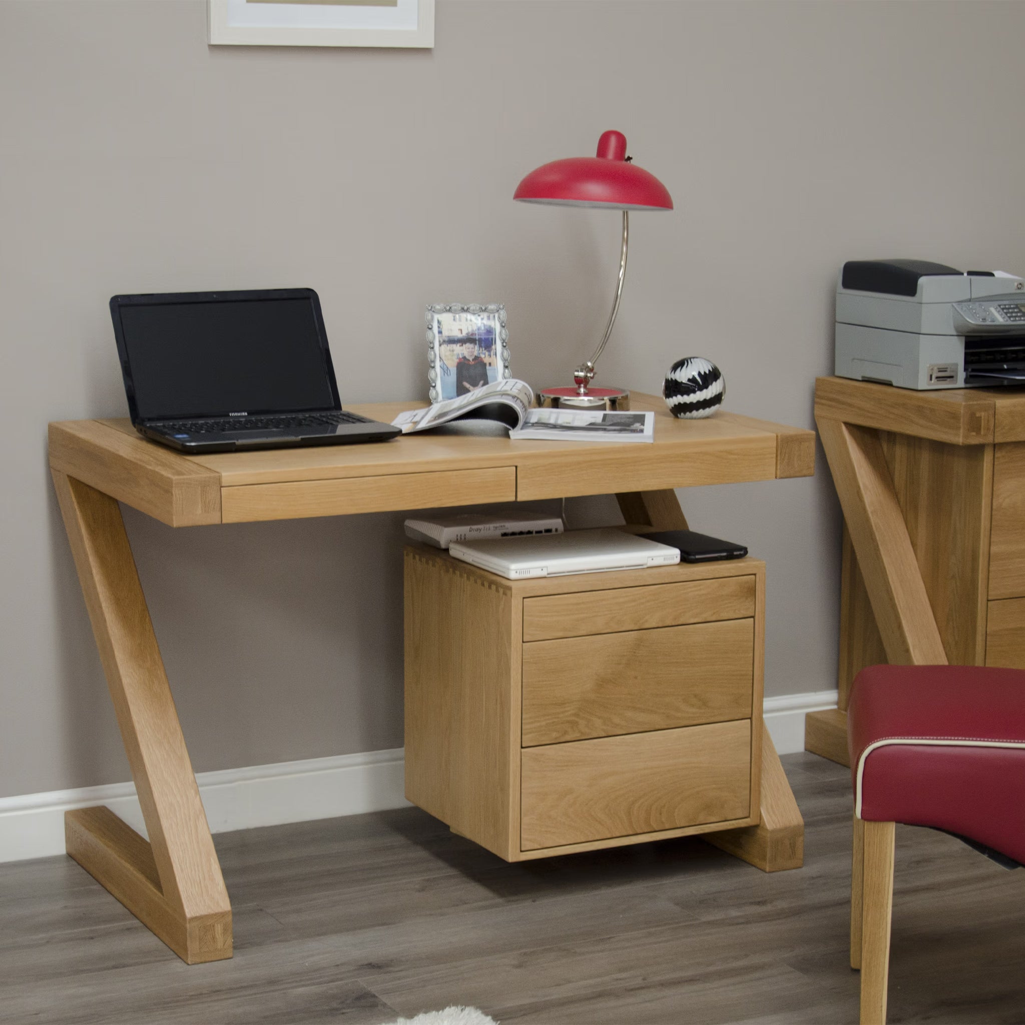Oak office desk with drawers, laptop, red desk lamp and modern decor on wood floor
