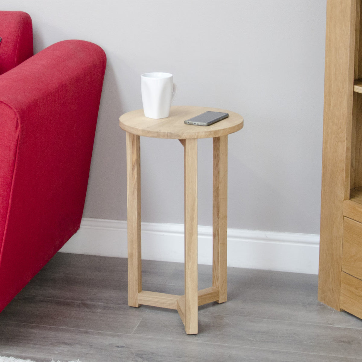 Oak side table beside red sofa with white mug and smartphone on tabletop