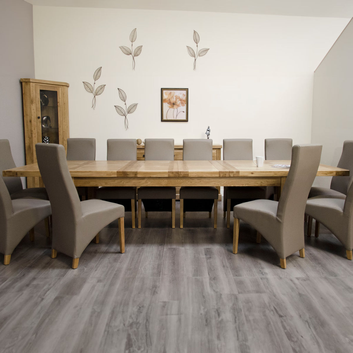 Large oak dining table with twelve beige upholstered chairs on grey wood floor