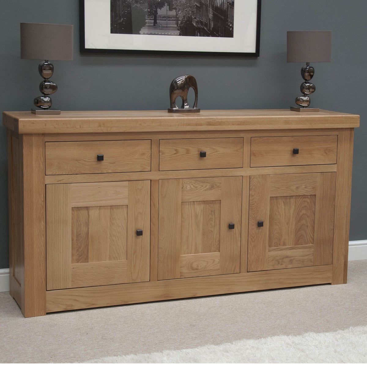 Oak sideboard with three drawers, three doors, black handles, and lamps on top