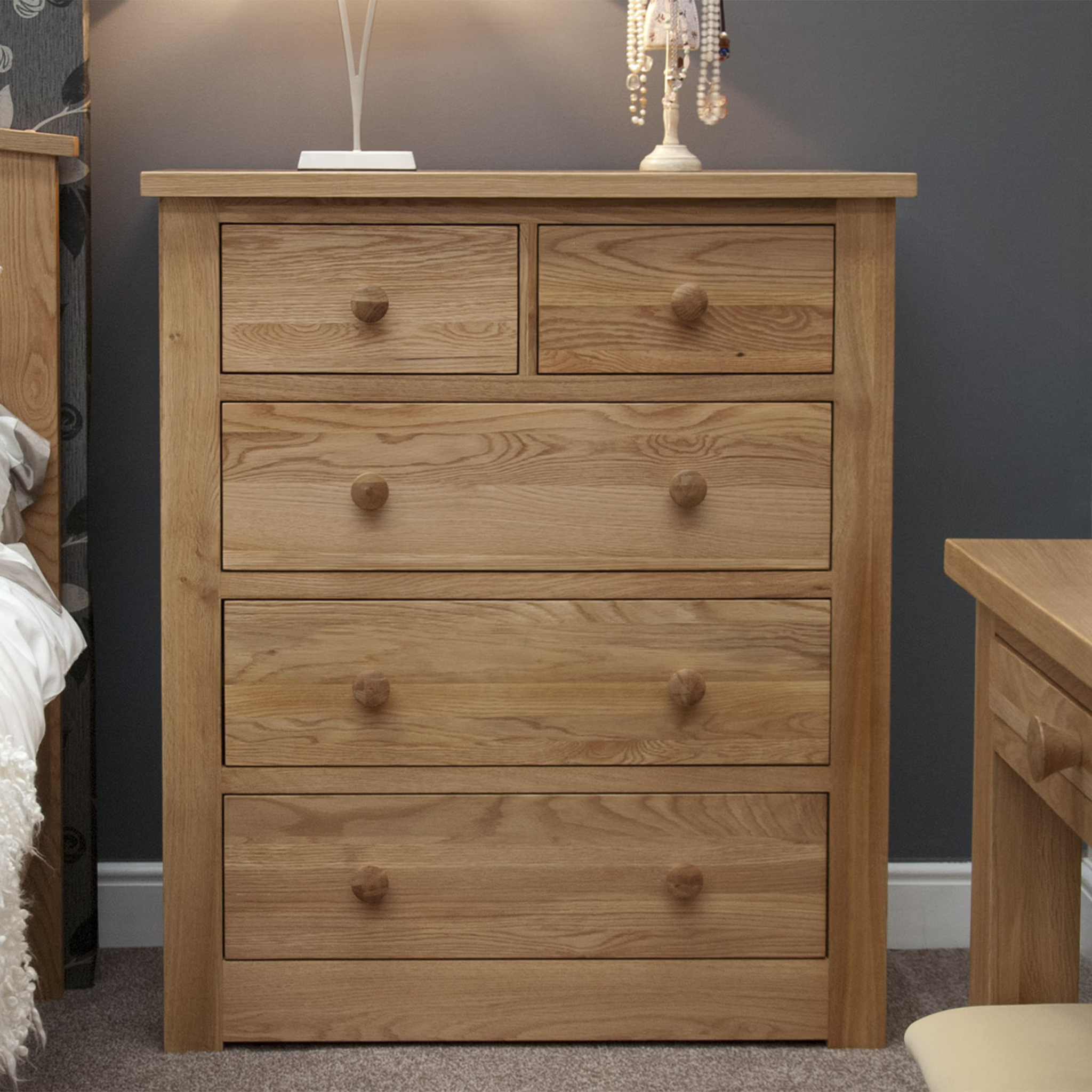Oak chest of drawers with five drawers and wooden knobs in a bedroom setting