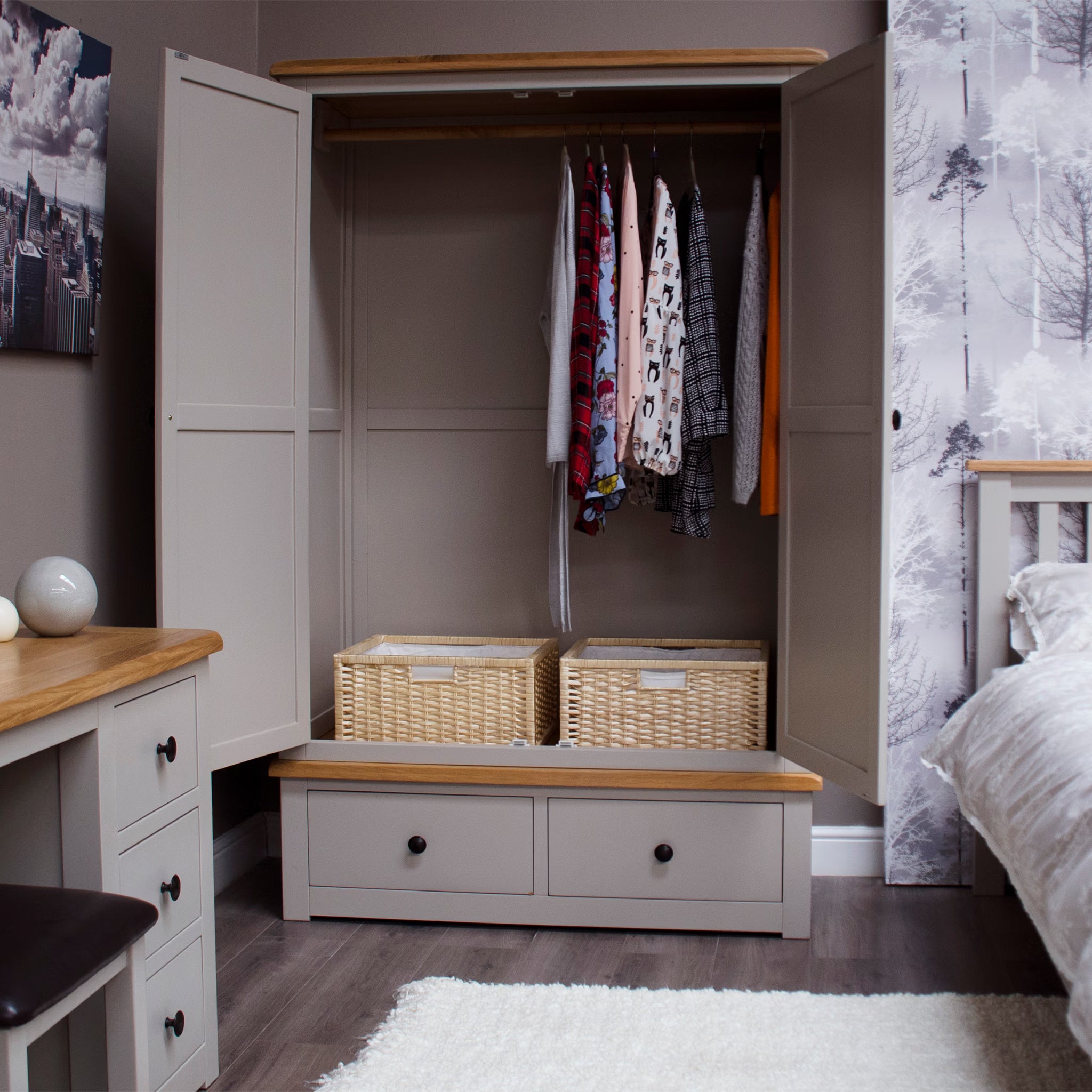 Grey wooden wardrobe with open doors, hanging clothes, wicker baskets, and two drawers
