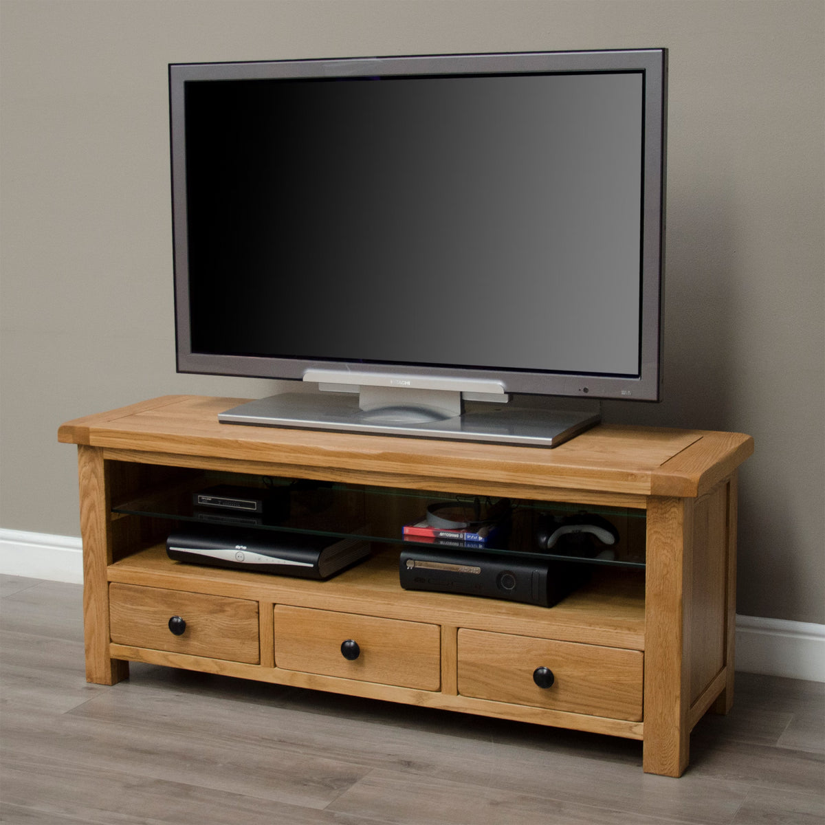 Oak TV unit with three drawers and open shelf holding consoles and remotes