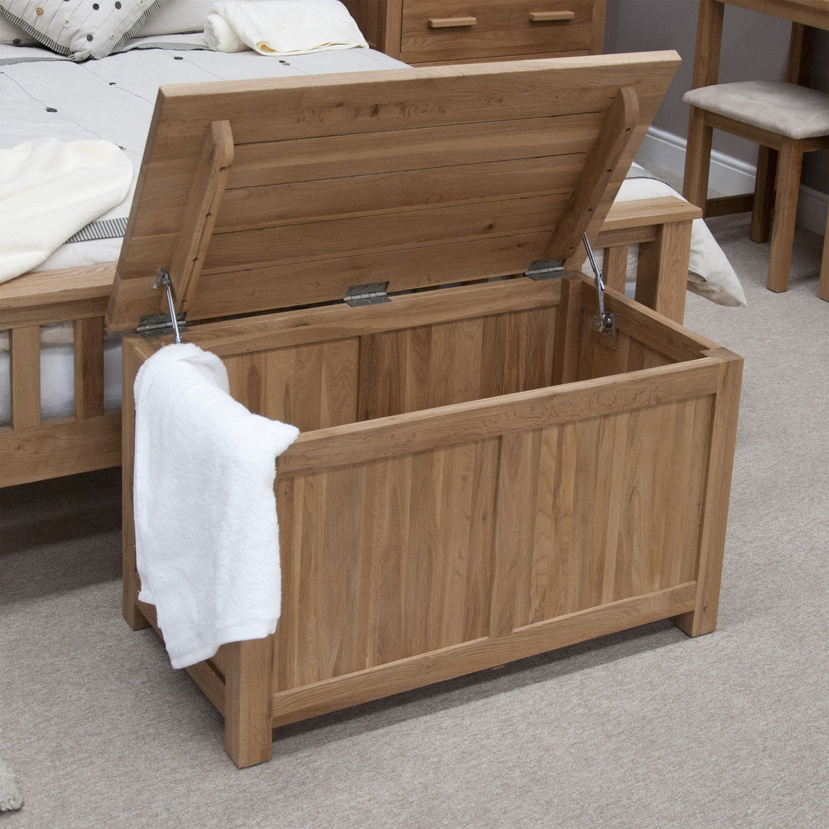 Oak wooden blanket box with open lid at the foot of a bed in a carpeted bedroom