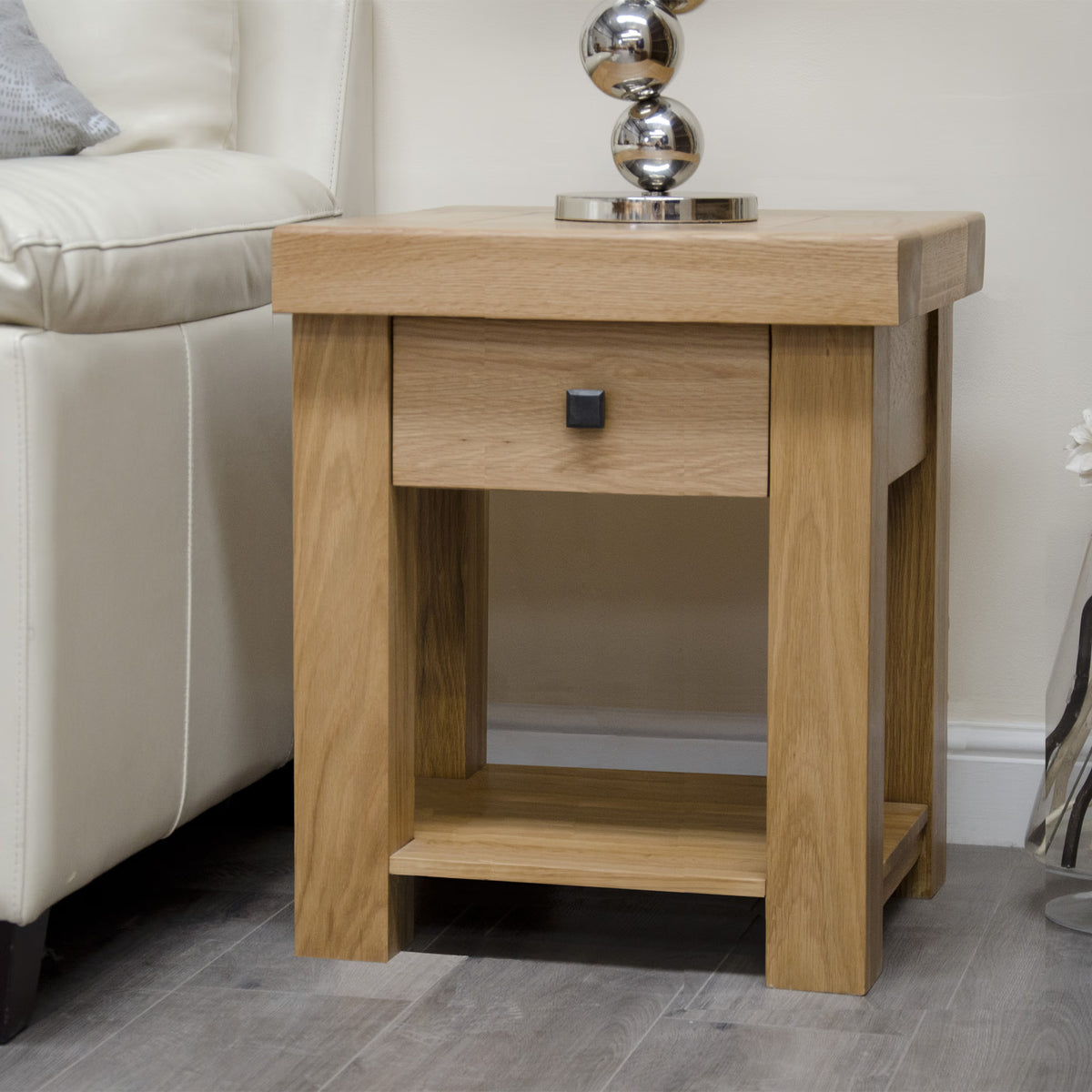Oak side table with single drawer and lower shelf beside cream sofa on wood floor