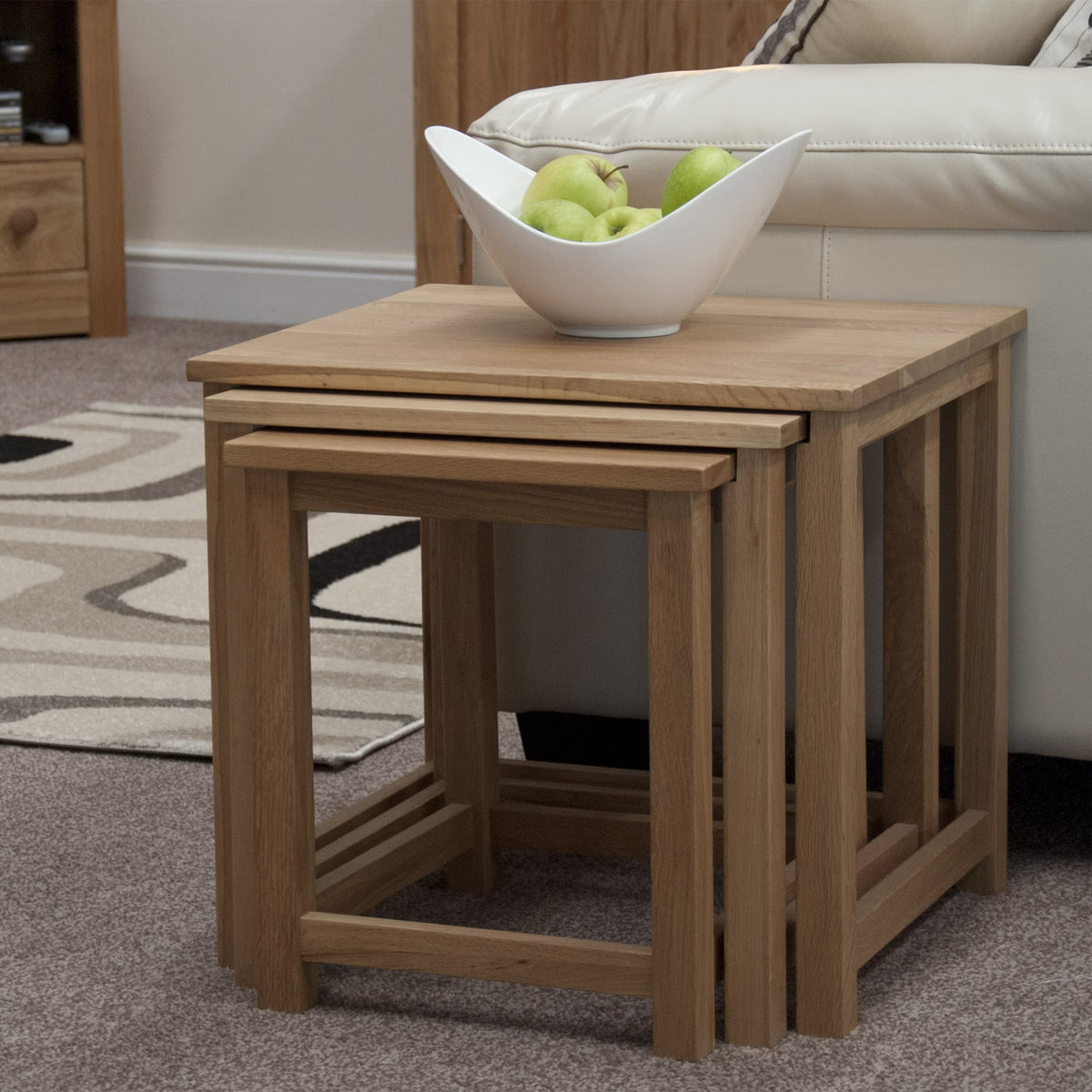 Oak nesting tables set beside sofa with white bowl of green apples