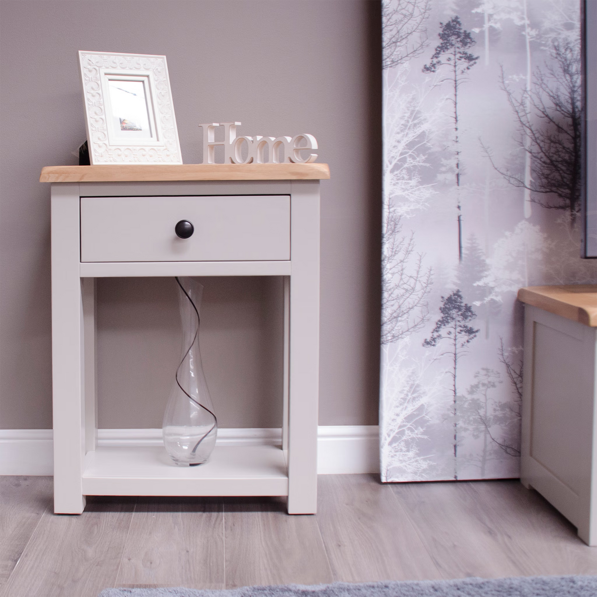 Light grey wooden bedside table with oak top, single drawer, lower shelf and decorative items
