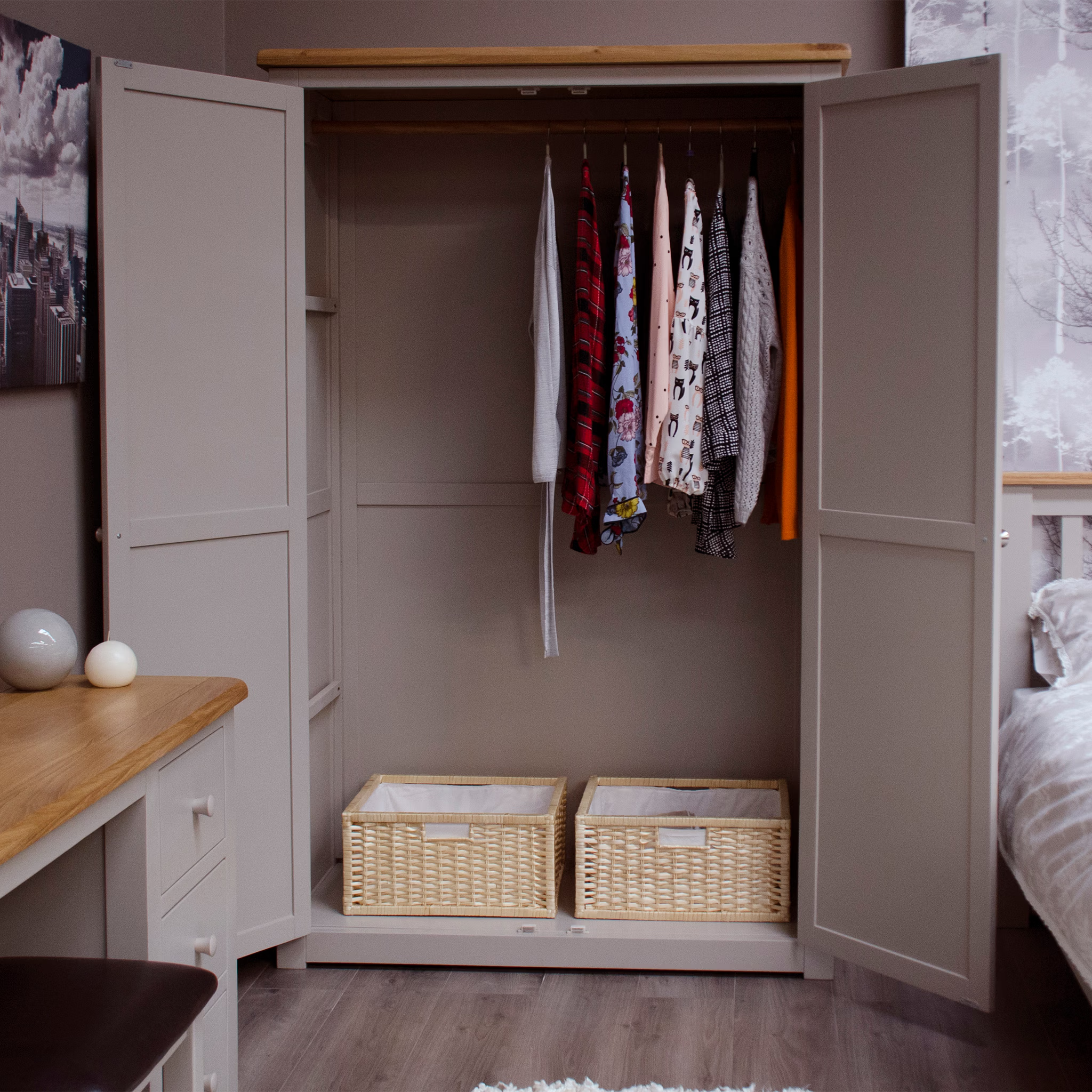 Beige wooden wardrobe with hanging clothes and two wicker storage baskets inside