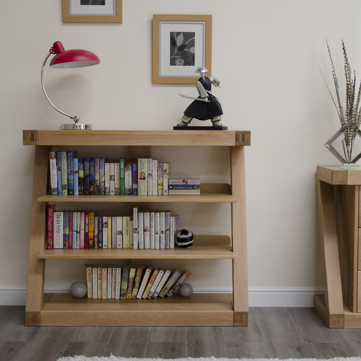 Oak bookcase with three shelves holding books, table lamp, and decorative ornaments