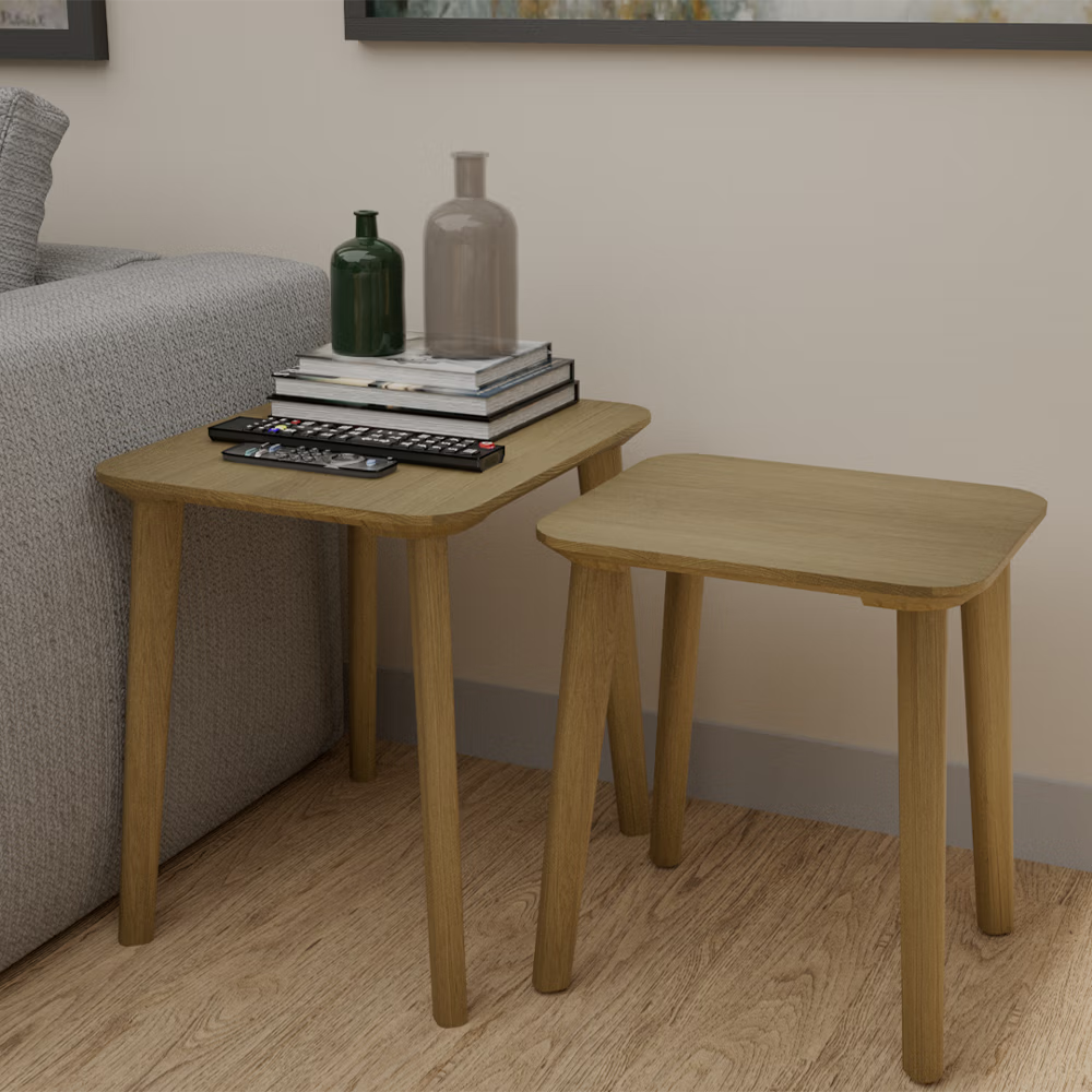 Oak nesting tables beside sofa with books, remotes, and decorative vases