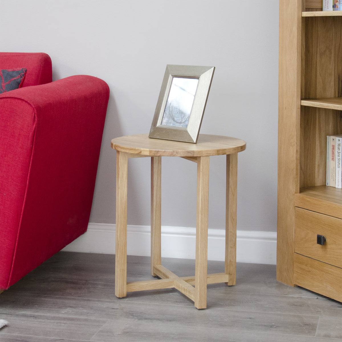 Light oak side table with round top beside a red sofa and wooden bookcase