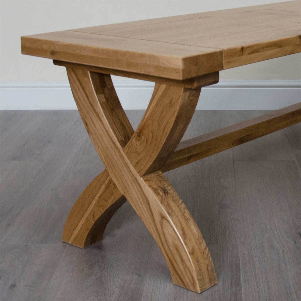 Solid oak dining table with cross leg base on laminate wood flooring