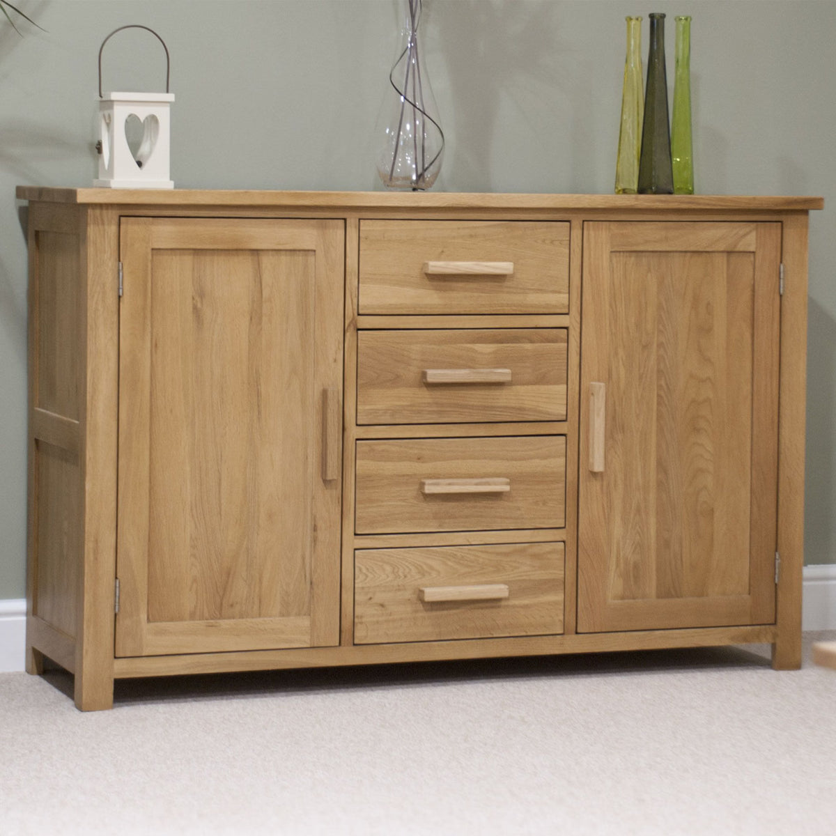 Oak sideboard with four drawers and two doors on beige carpet against light green wall