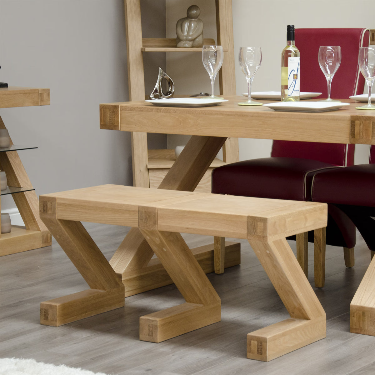 Oak dining bench with modern Z-shaped legs beside matching table and red chairs