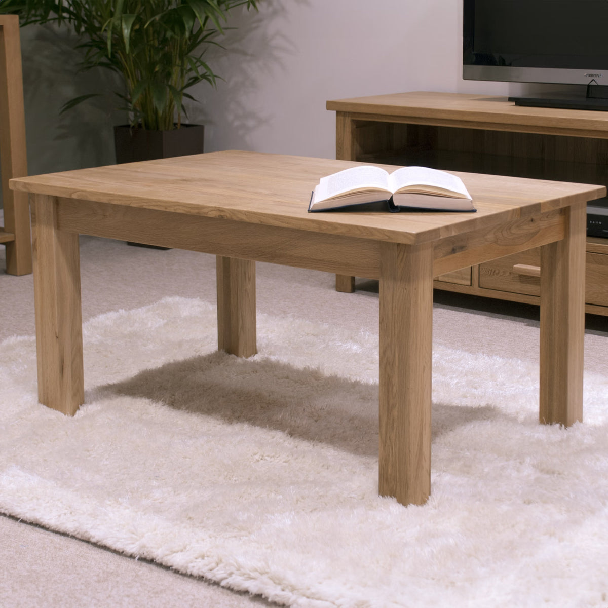 Oak coffee table with open book on cream rug in living room