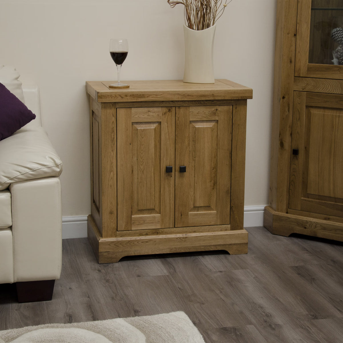 Oak sideboard with two doors, black handles, vase and wine glass, in living room