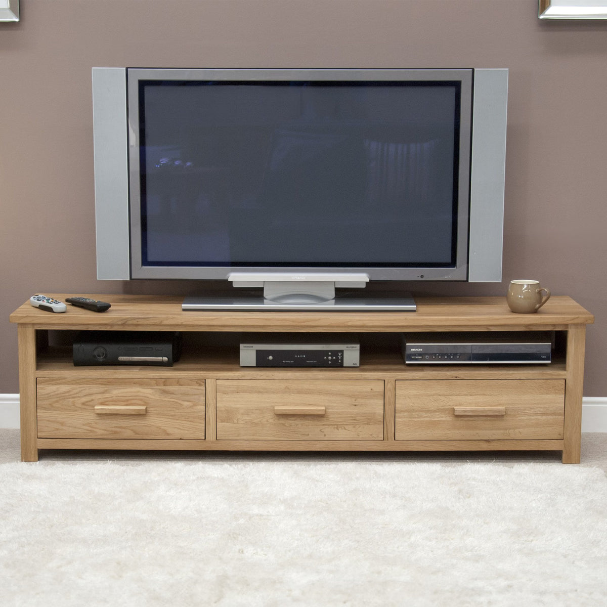 Oak TV unit with three drawers, open shelf holding electronics, flat-screen TV on top