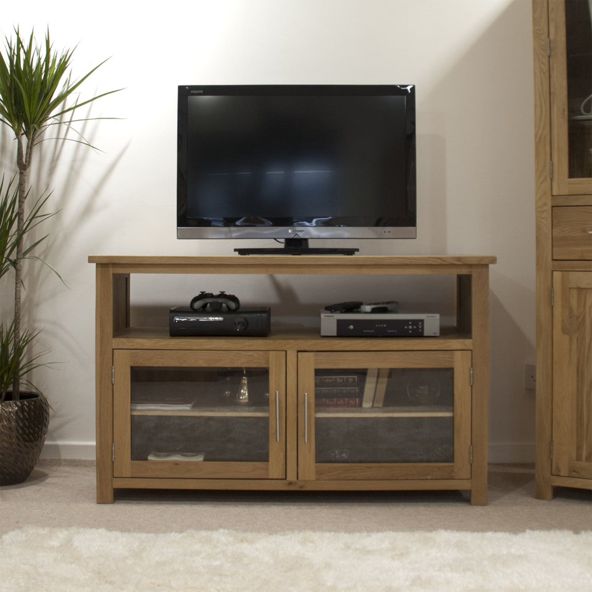 Oak TV unit with glass cabinet doors and open shelf, shown with electronics and decor