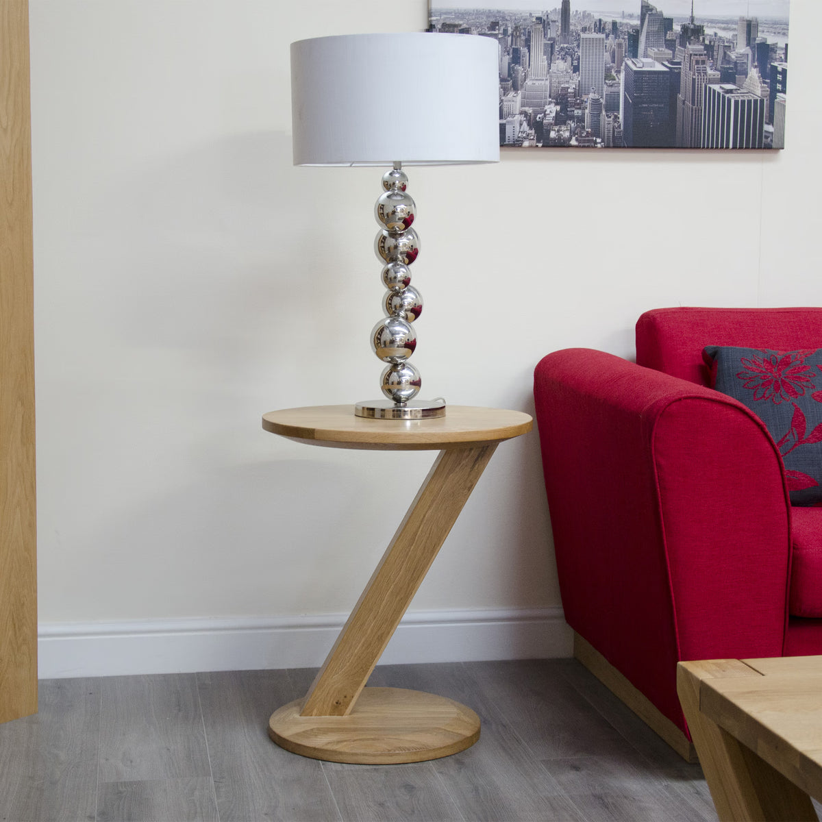 Oak Z-shaped side table with modern silver lamp beside red sofa on wood floor