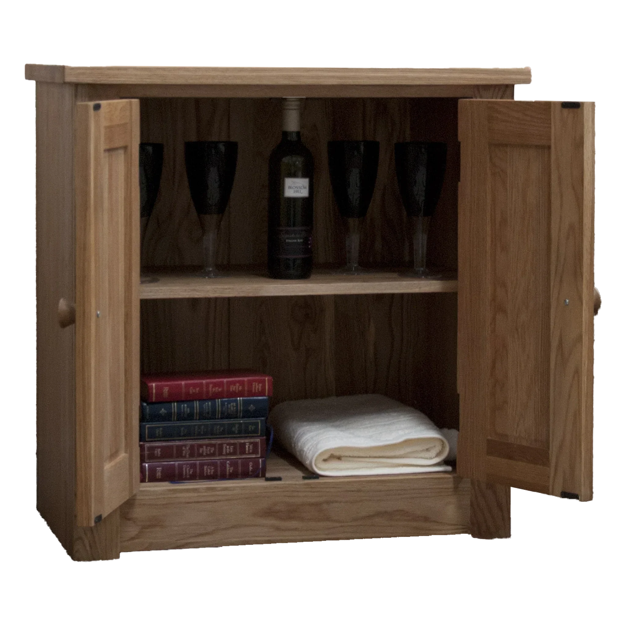 Oak sideboard cabinet with open doors, shelves holding wine glasses, bottle, books, towel