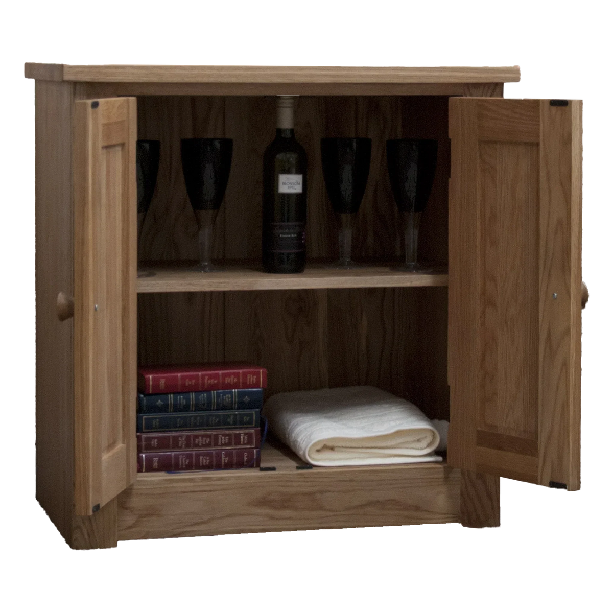 Oak sideboard cabinet with open doors, shelves holding wine glasses, bottle, books, towel