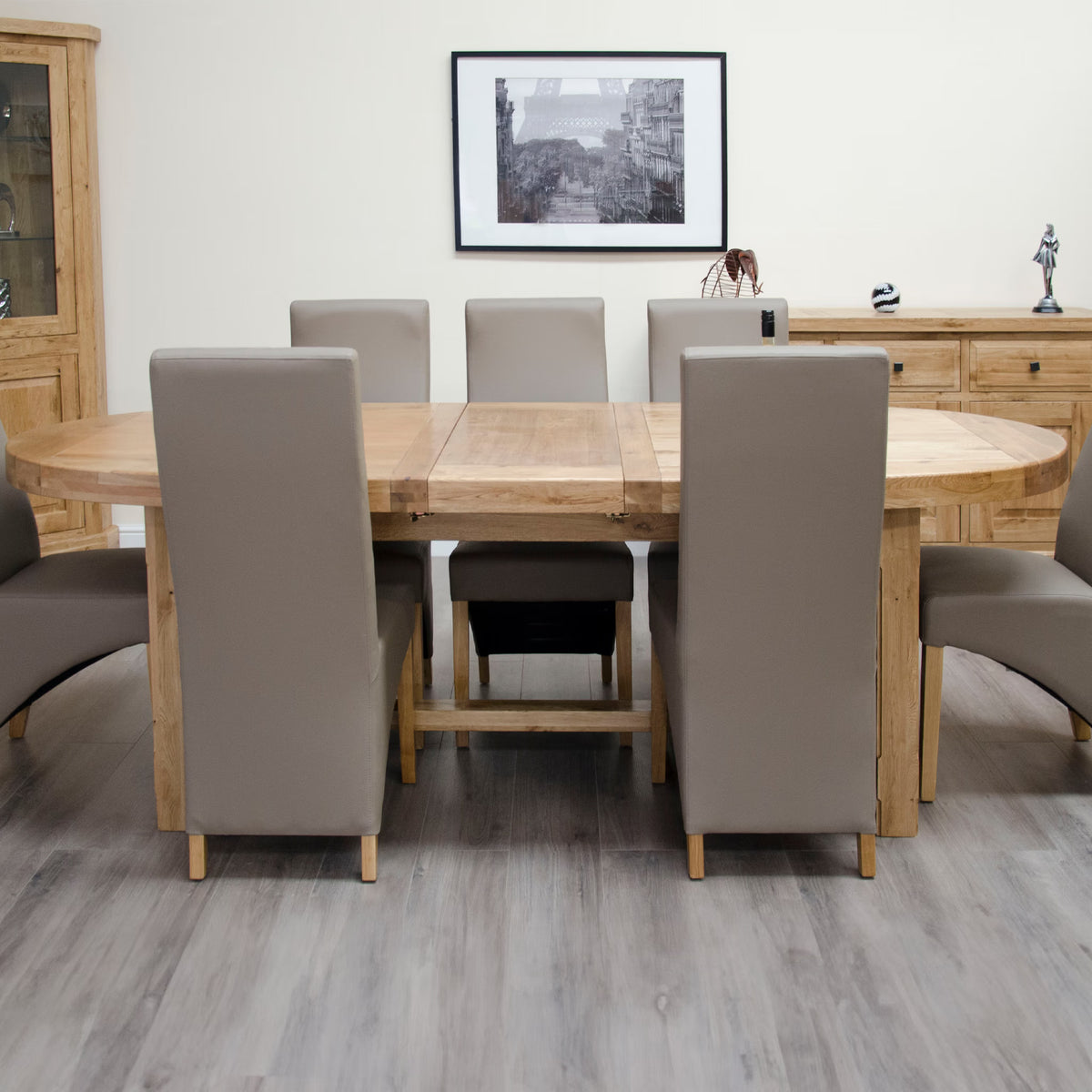 Oak dining table with six taupe upholstered chairs on grey wood floor