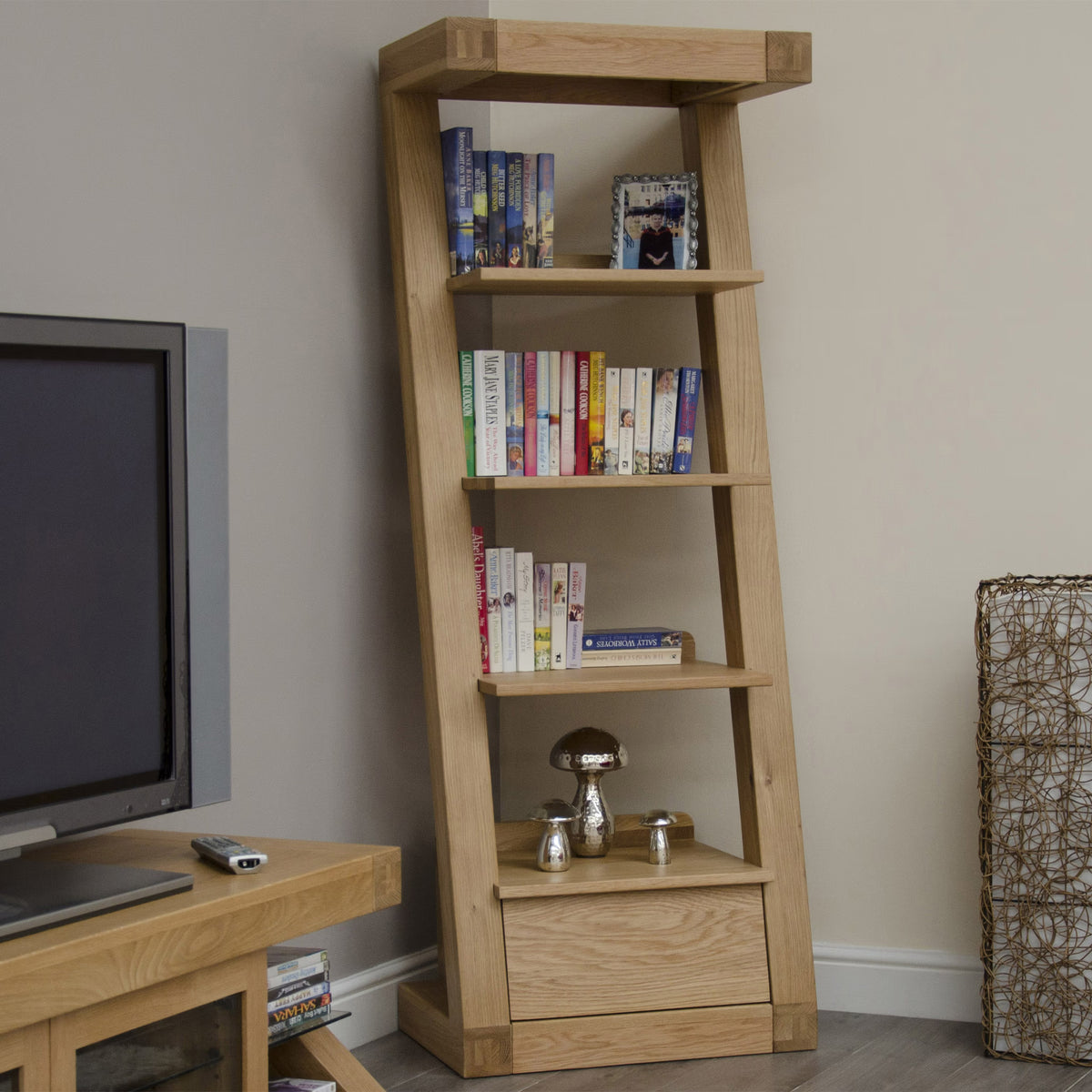 Oak ladder bookshelf with shelving and drawer holding books and decor against wall