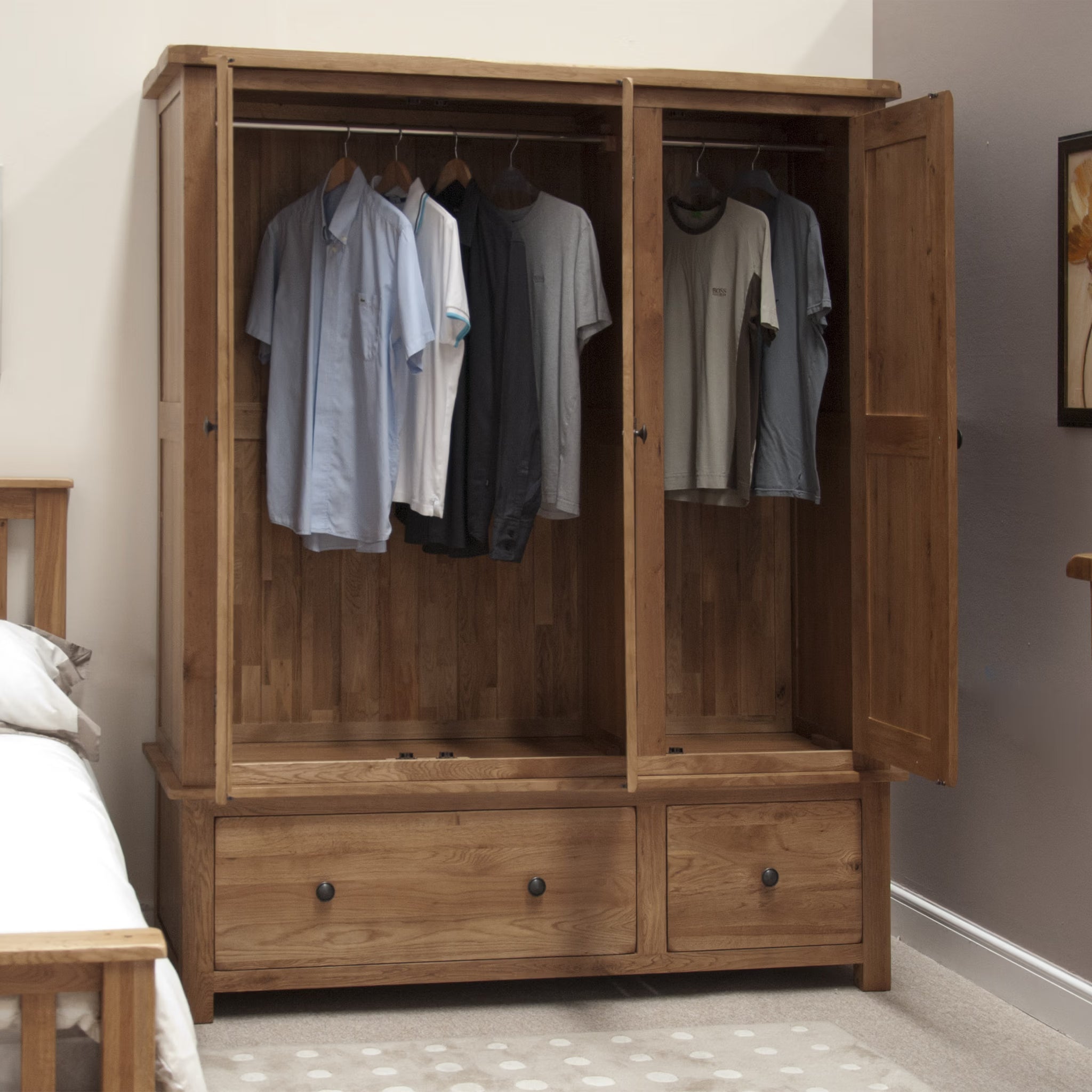 Wooden wardrobe with open doors, hanging clothes, and two drawers in bedroom setting