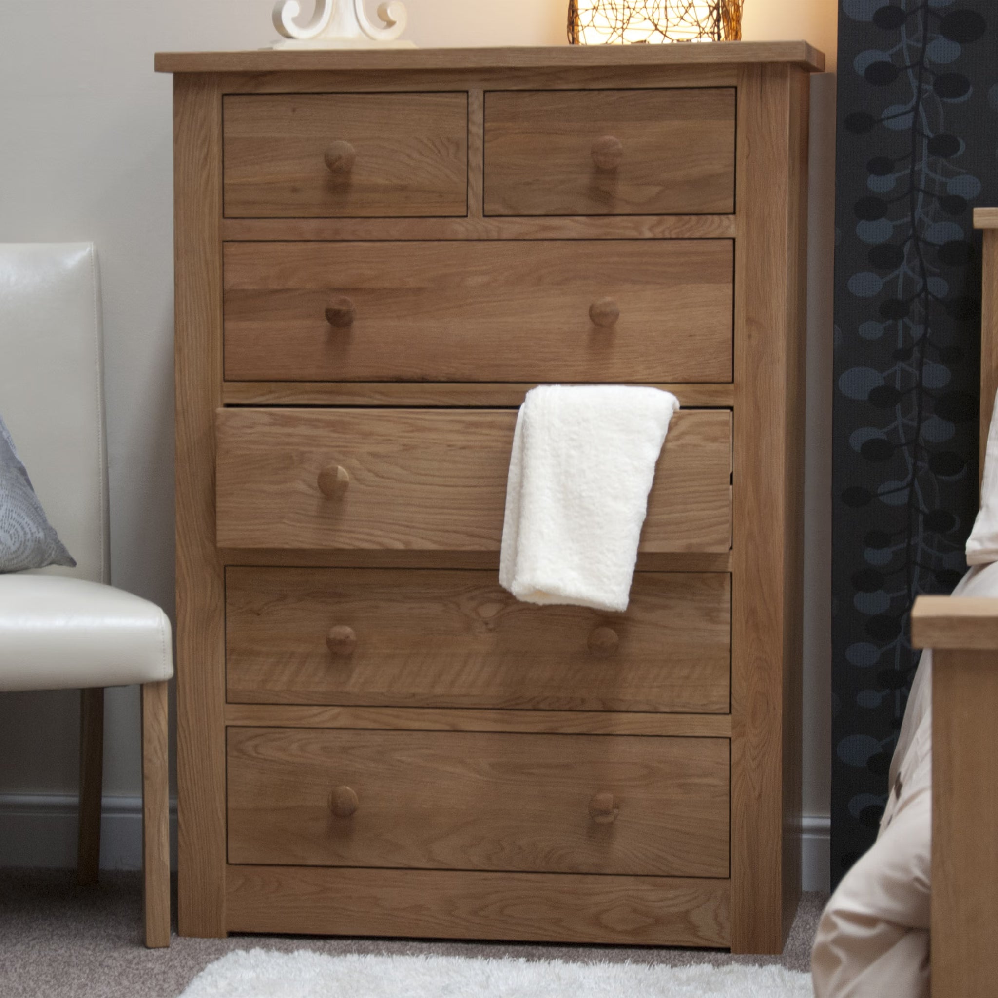 Oak chest of drawers with six storage drawers in a bedroom setting
