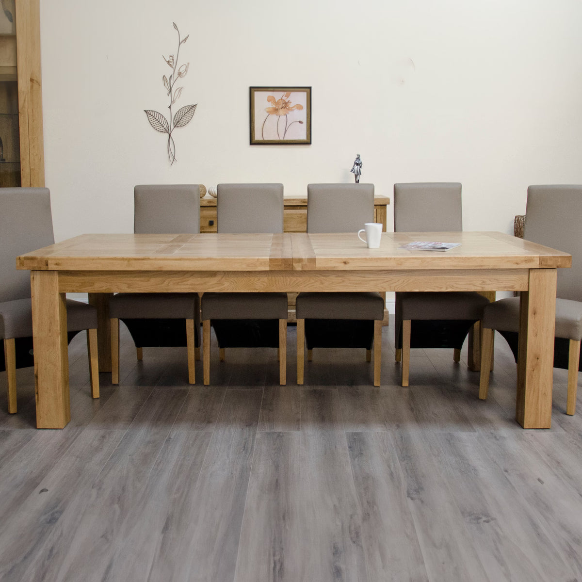 Large oak dining table with eight grey upholstered chairs in a modern dining room setting