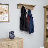 Oak wall coat rack with five metal hooks holding two jackets in modern hallway