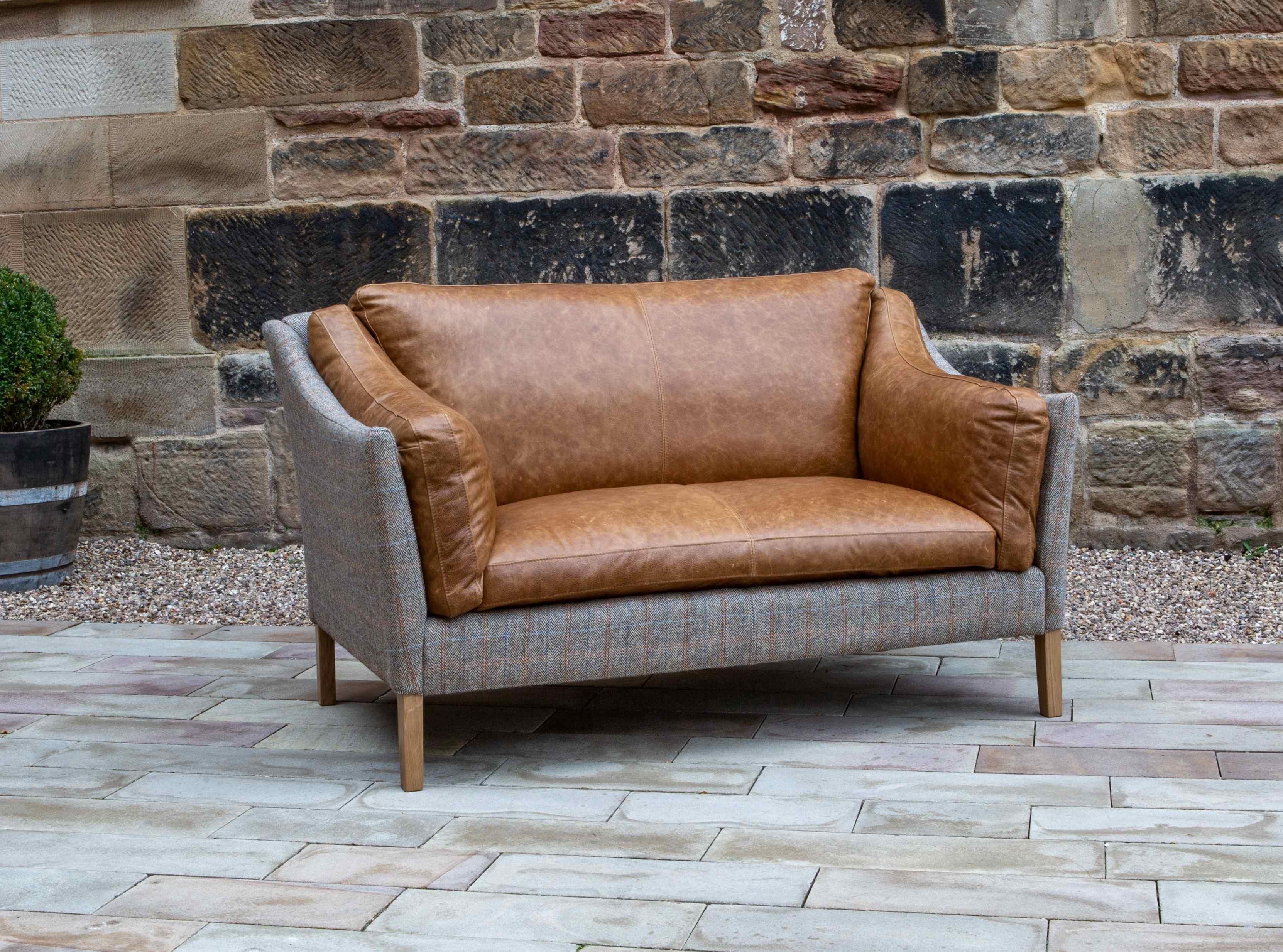 Two-seater brown leather and grey fabric sofa with wooden legs on outdoor patio
