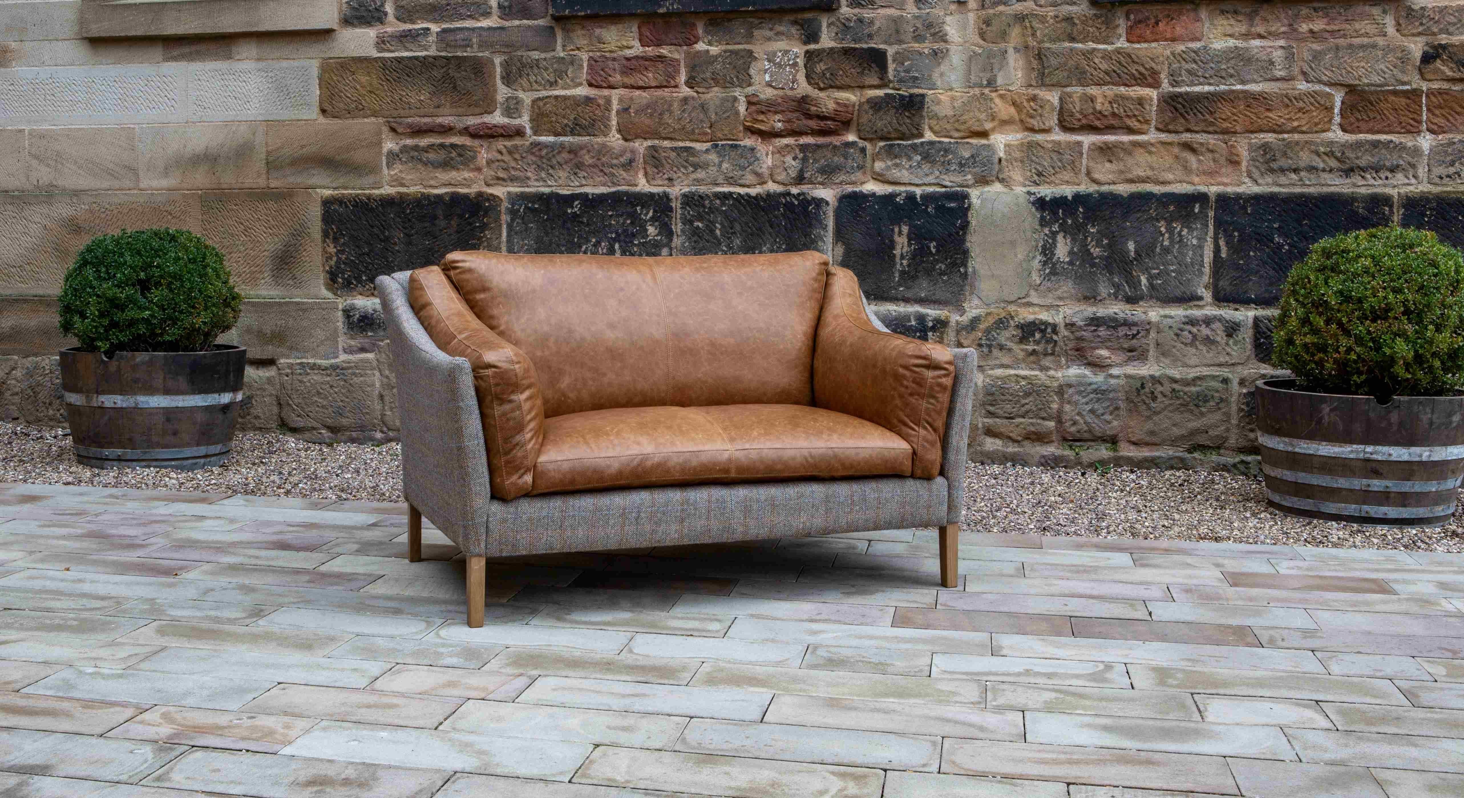 Brown leather and grey fabric loveseat sofa on patio with brick wall backdrop