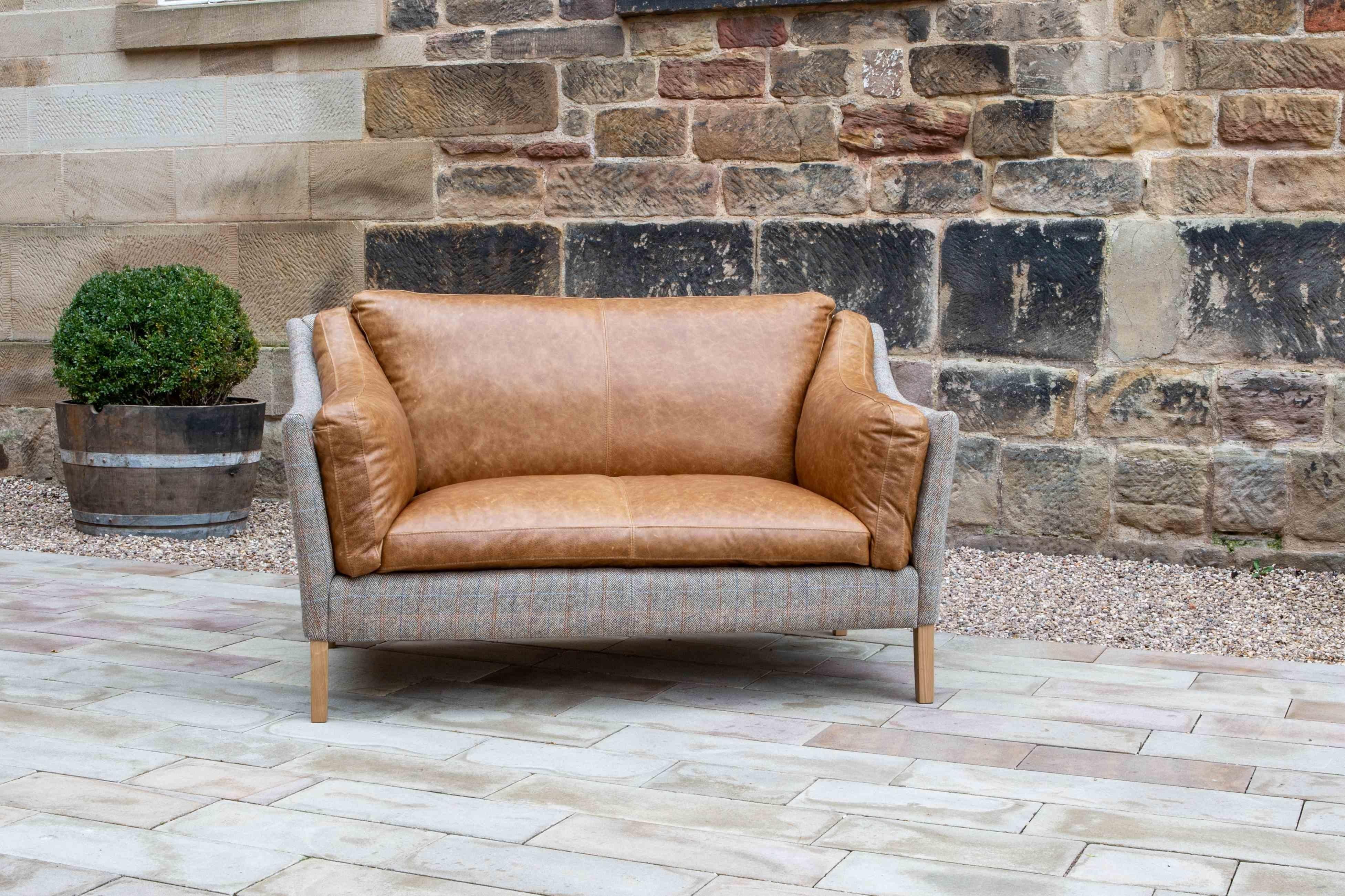 Tan leather two seater sofa with fabric sides and wooden legs on a stone patio