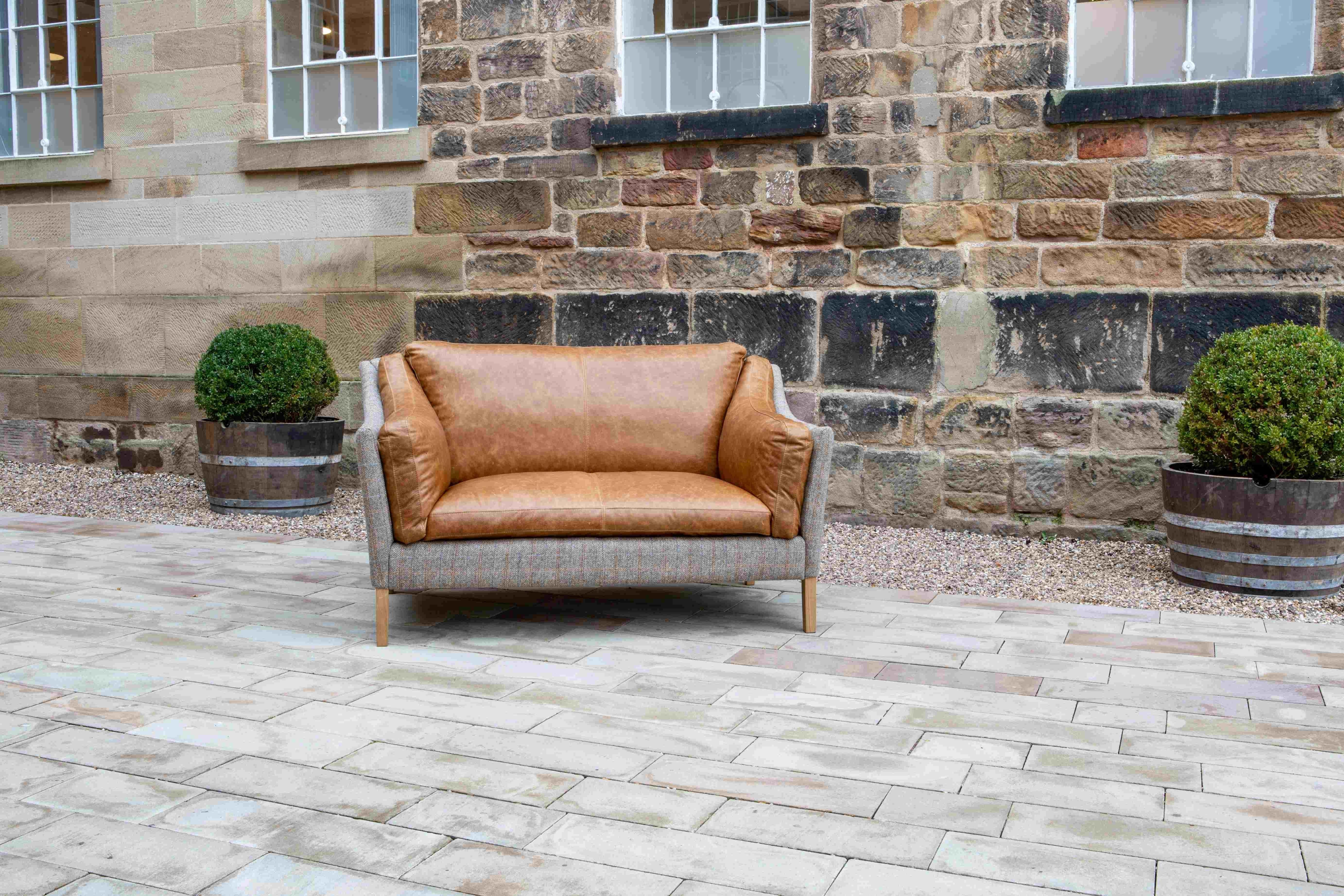Tan leather two-seater sofa with wooden legs on stone patio, outdoor setting