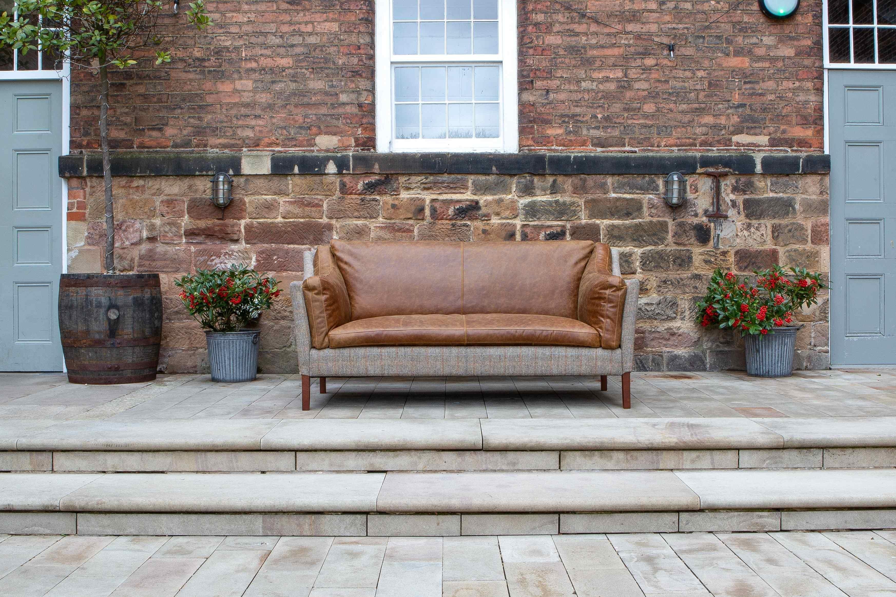 Brown leather and fabric sofa on stone patio with potted plants and brick wall backdrop
