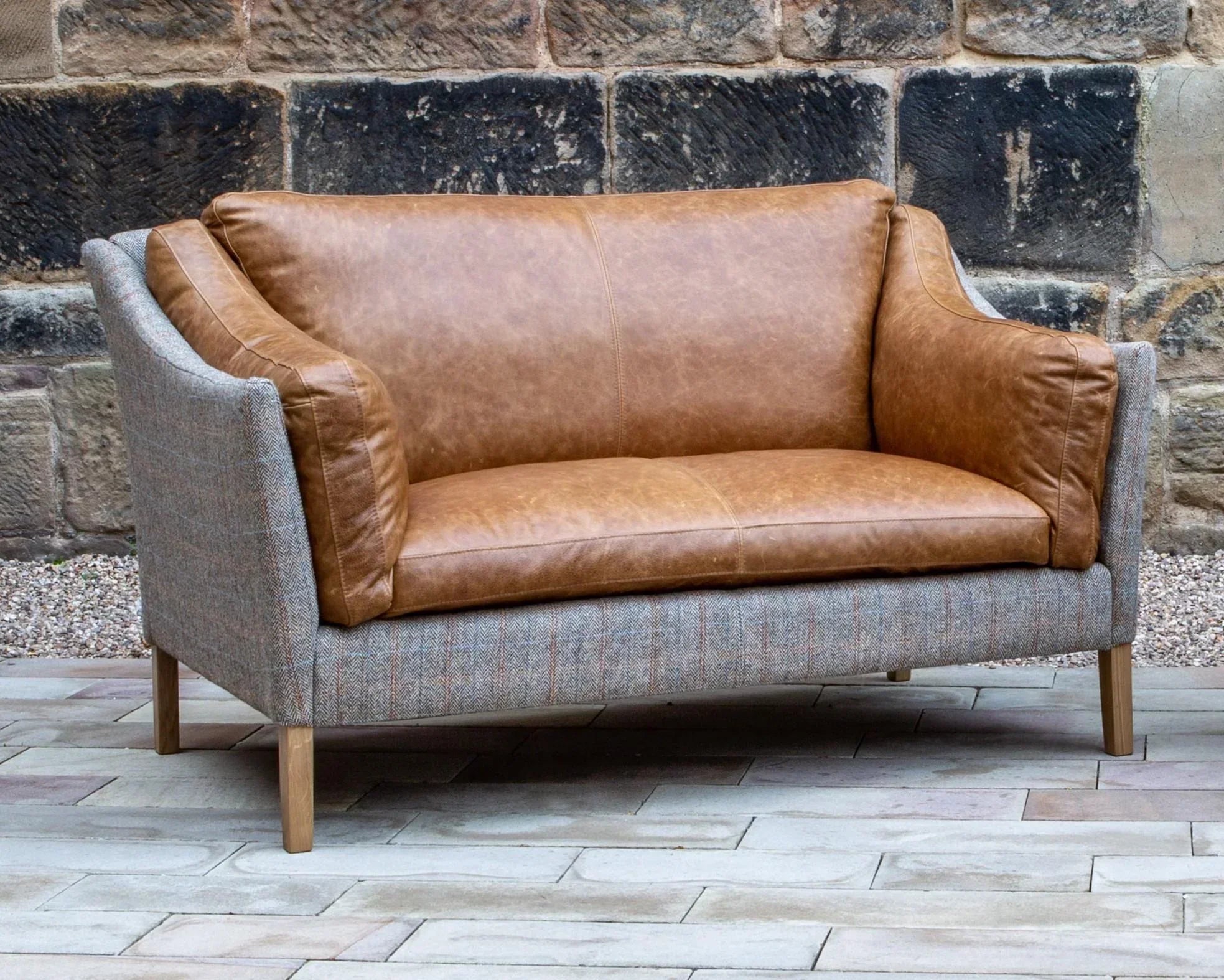 Tan leather and grey fabric sofa with wooden legs set outdoors on patio