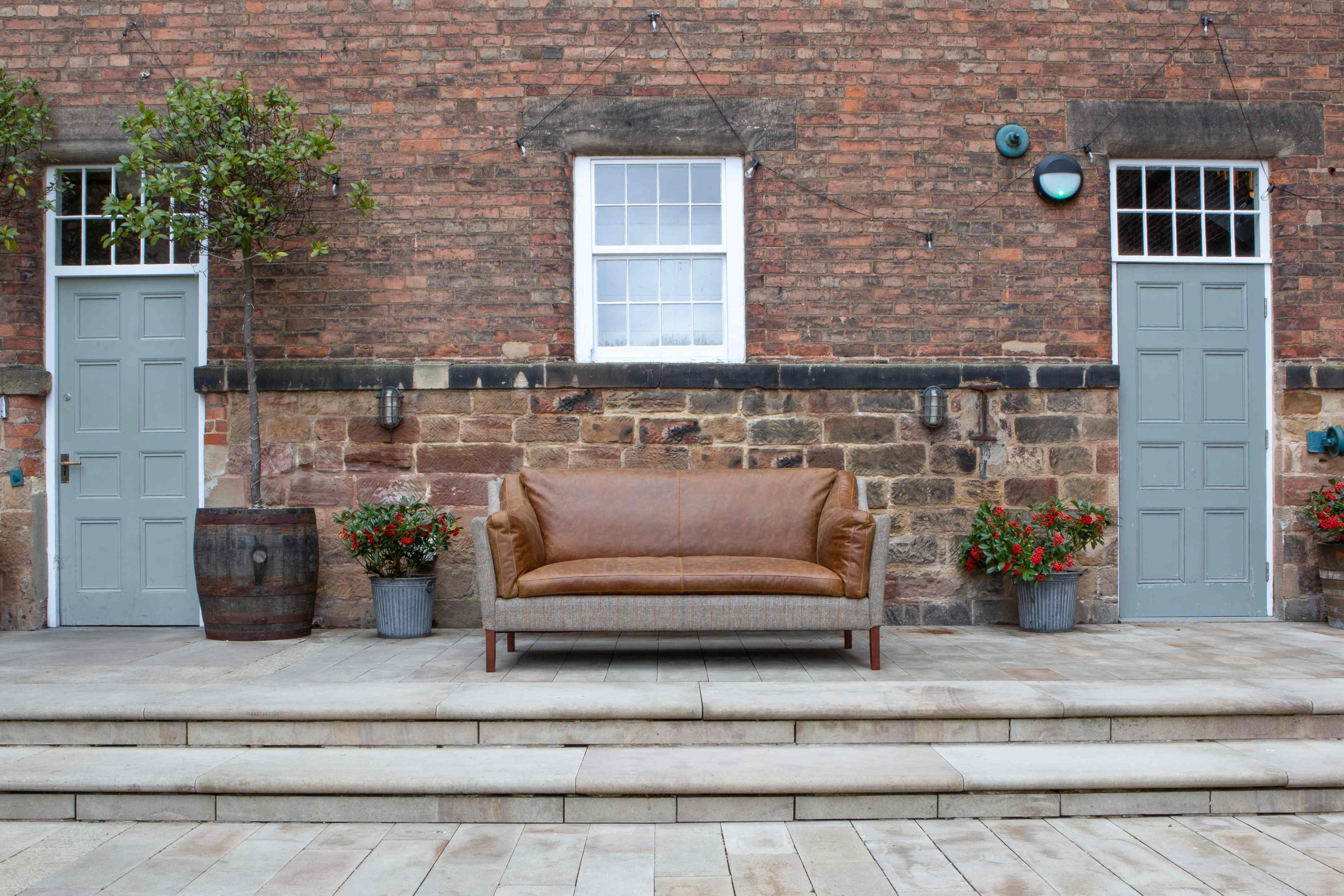 Brown leather and grey fabric sofa on a patio in front of a brick house with blue doors